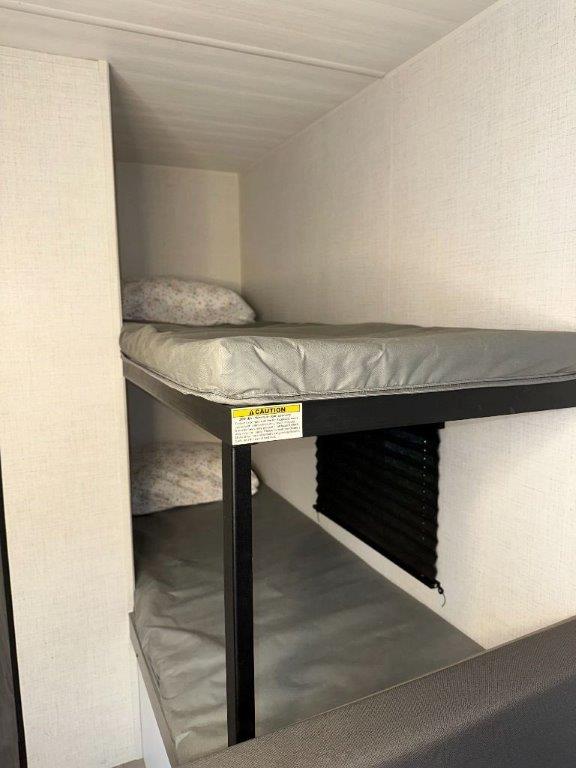 Compact bunk beds with grey mattresses provide sleeping space in this RV rental. A caution sticker is on the upper bunk frame.. Keystone RV Hideout Sport 2024