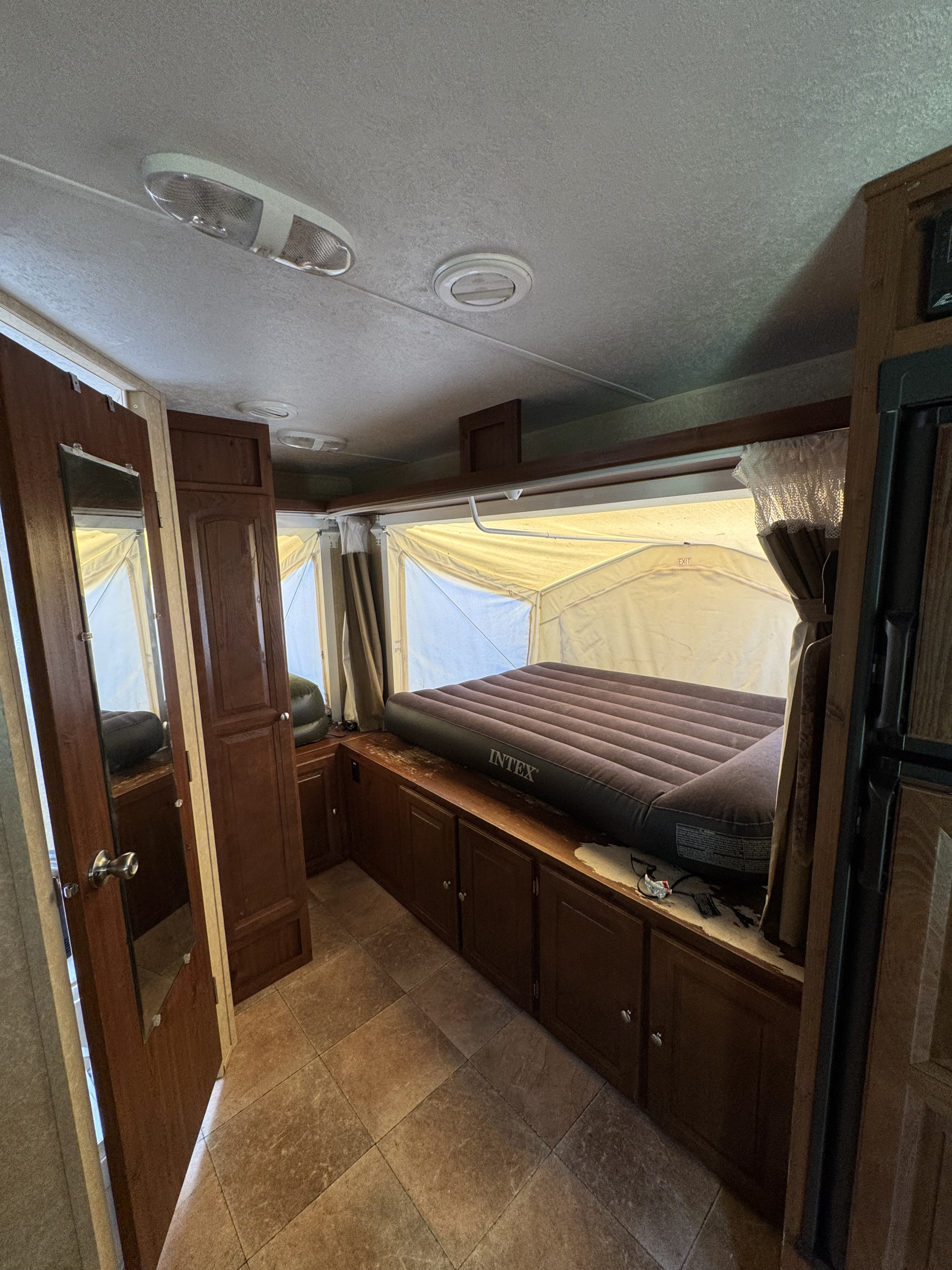 RV rental interior: cozy sleeping area with air mattress & storage in a pop-up camper. Tiled floor & wood cabinets.. Forest river Rockwood 2011