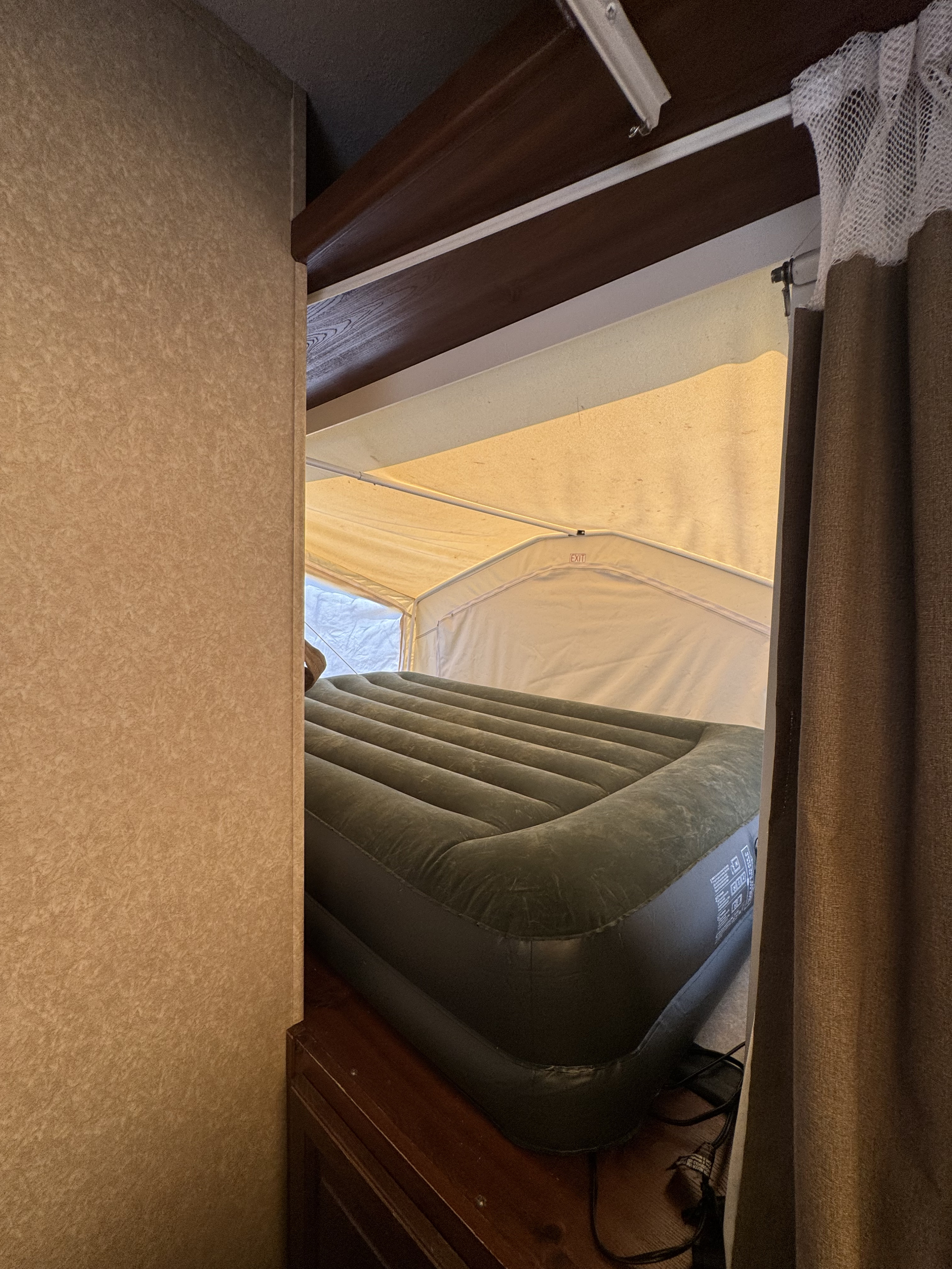 Inside an RV rental, an inflatable air mattress fills a pop-up camper bunk, with canvas walls and a brown curtain.. Forest river Rockwood 2011