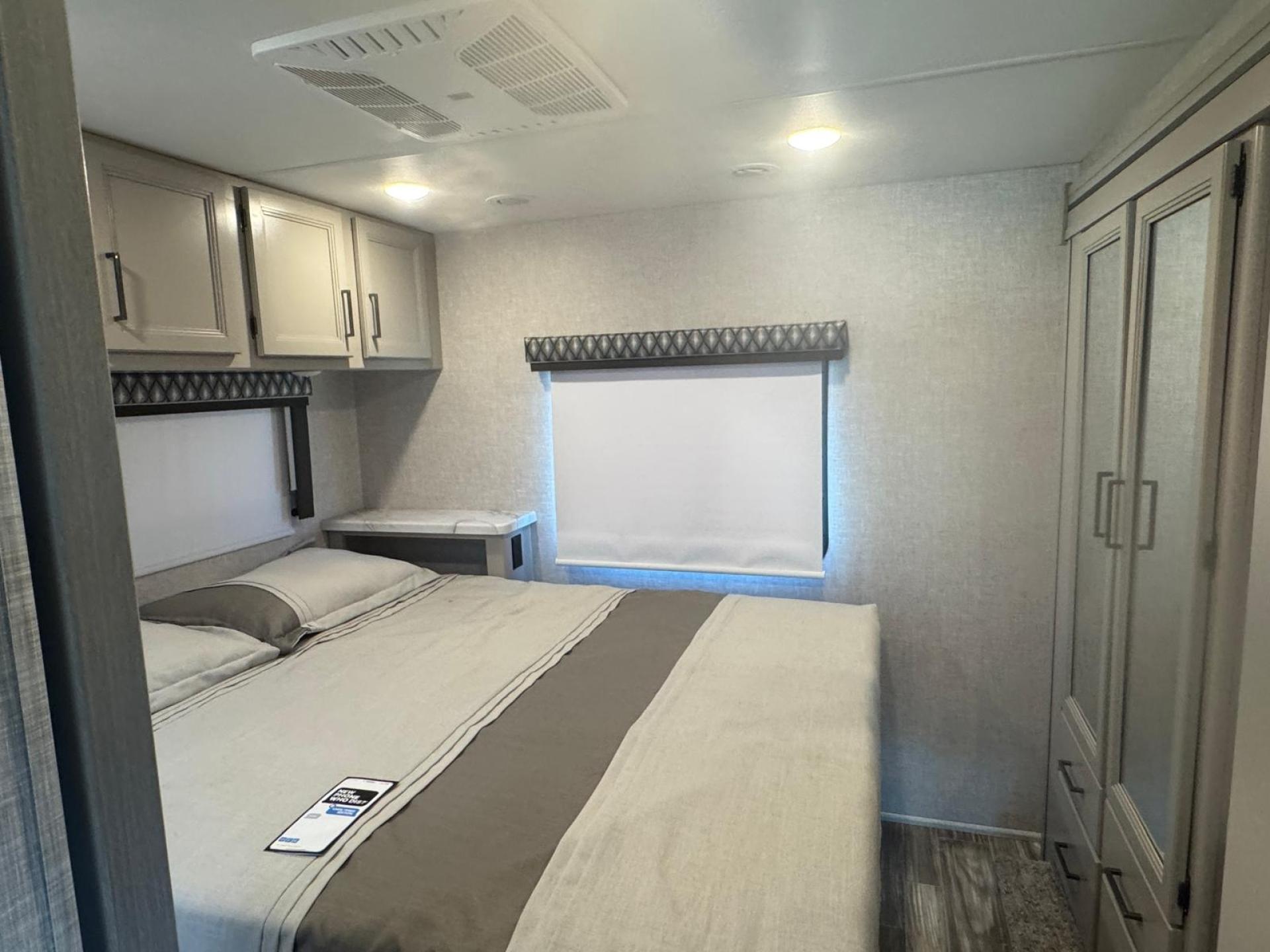 Modern RV rental bedroom interior with a bed, overhead storage, window, and wardrobe, offering comfort for your trip.. Thor Geneva 2025