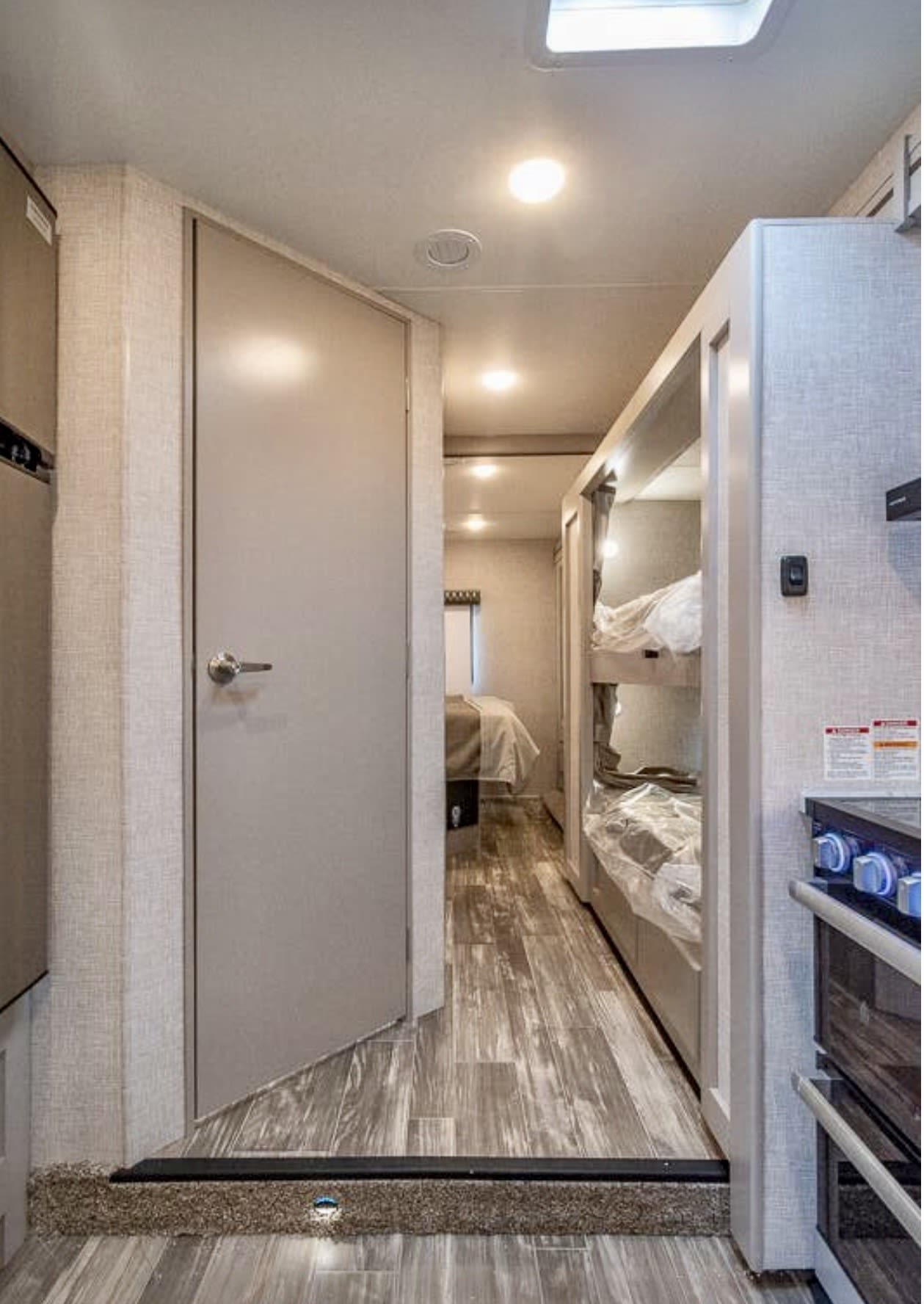 RV rental interior: bunk beds, kitchen stove, and a hallway leading to a bedroom through an open door. Wood flooring.. Thor Geneva 2025