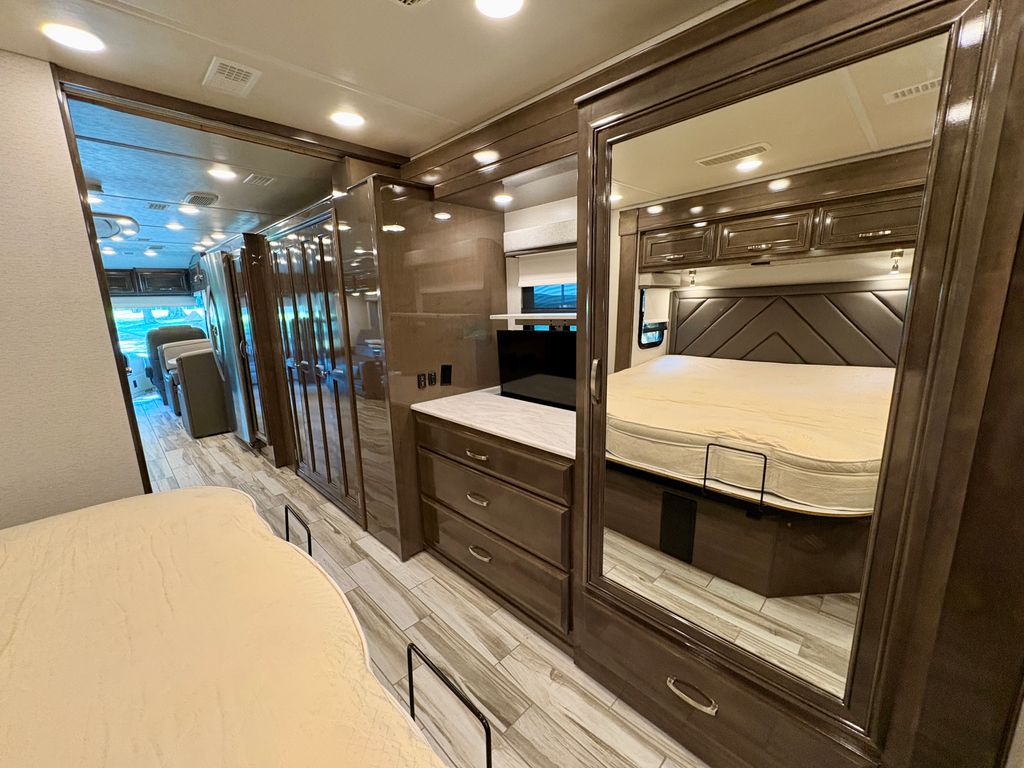 Modern RV rental: a master bedroom with mirrored wardrobe, additional bed, and view into the bright living area.. Entegra Coach Reatta 2022
