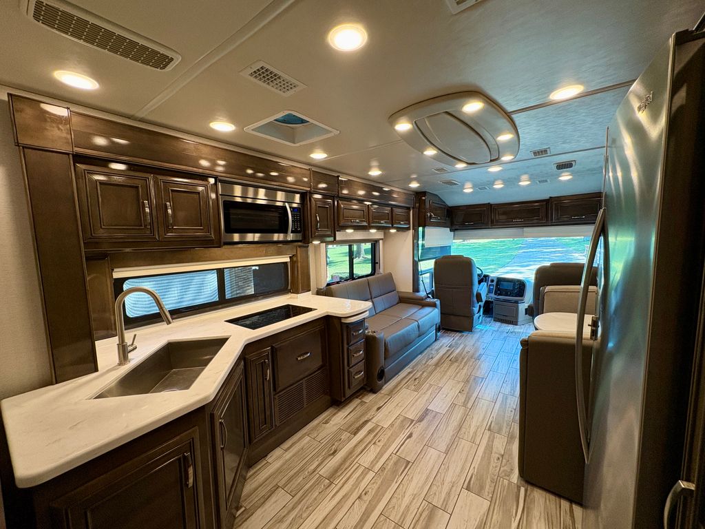 Modern RV rental interior: well-equipped kitchen with stainless steel appliances, dark cabinetry, and bright living space with sofa.. Entegra Coach Reatta 2022