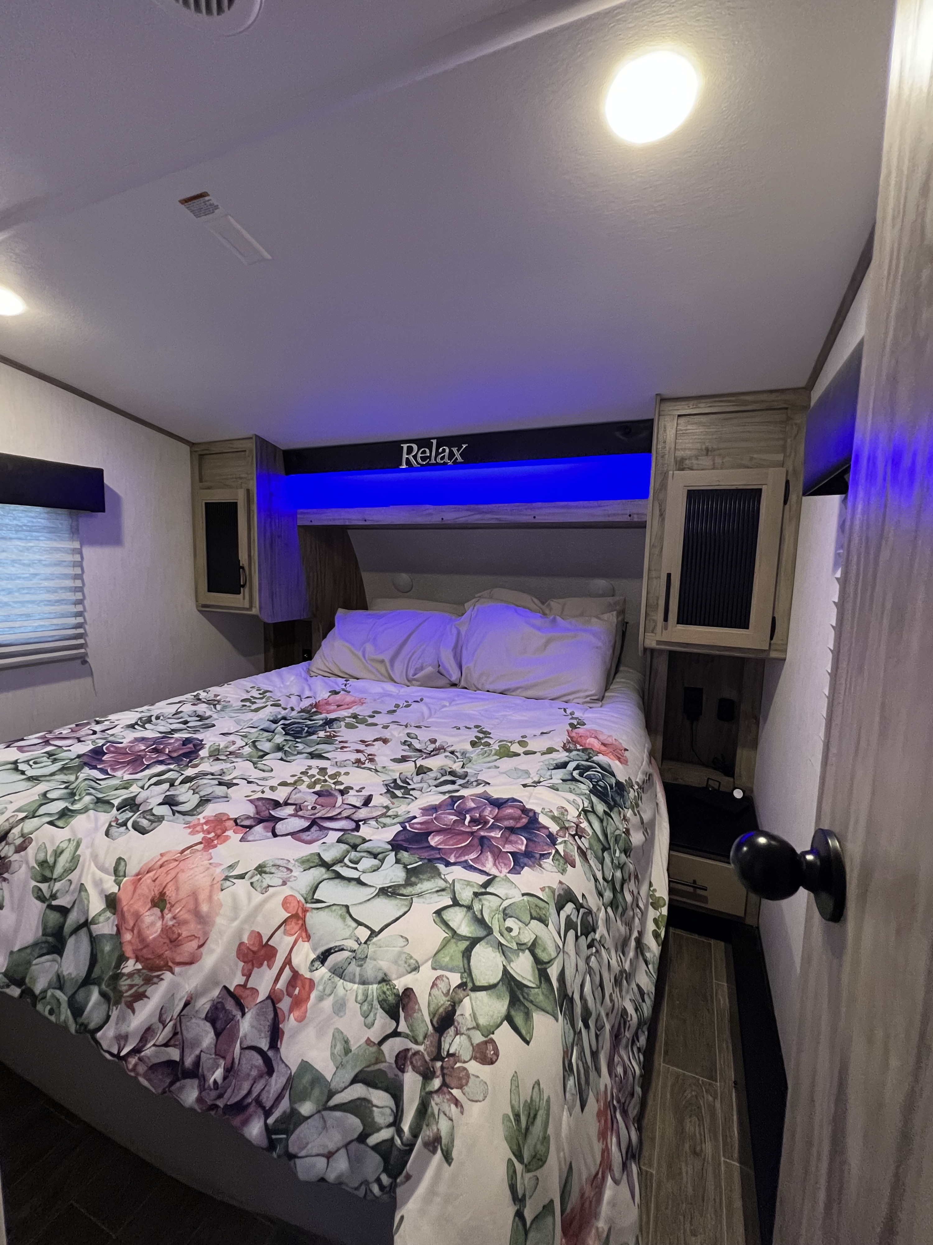 This cozy RV rental bedroom features a floral comforter, blue accent lights, and a "Relax" sign over the bed.. Forest River Cherokee Arctic Wolf 2021