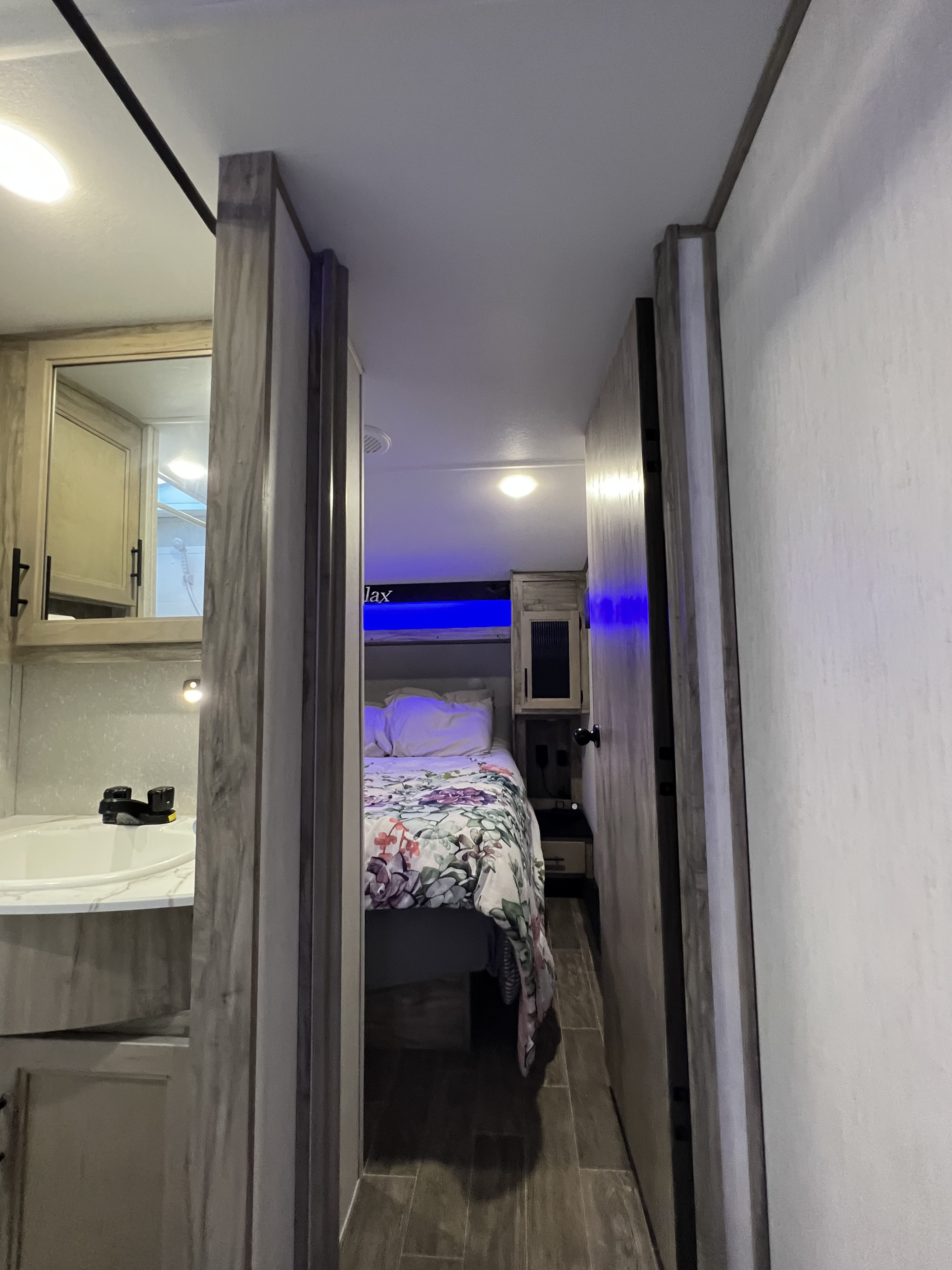 Interior of an RV rental: view from bathroom to bedroom with a floral bedspread & blue mood lighting.. Forest River Cherokee Arctic Wolf 2021
