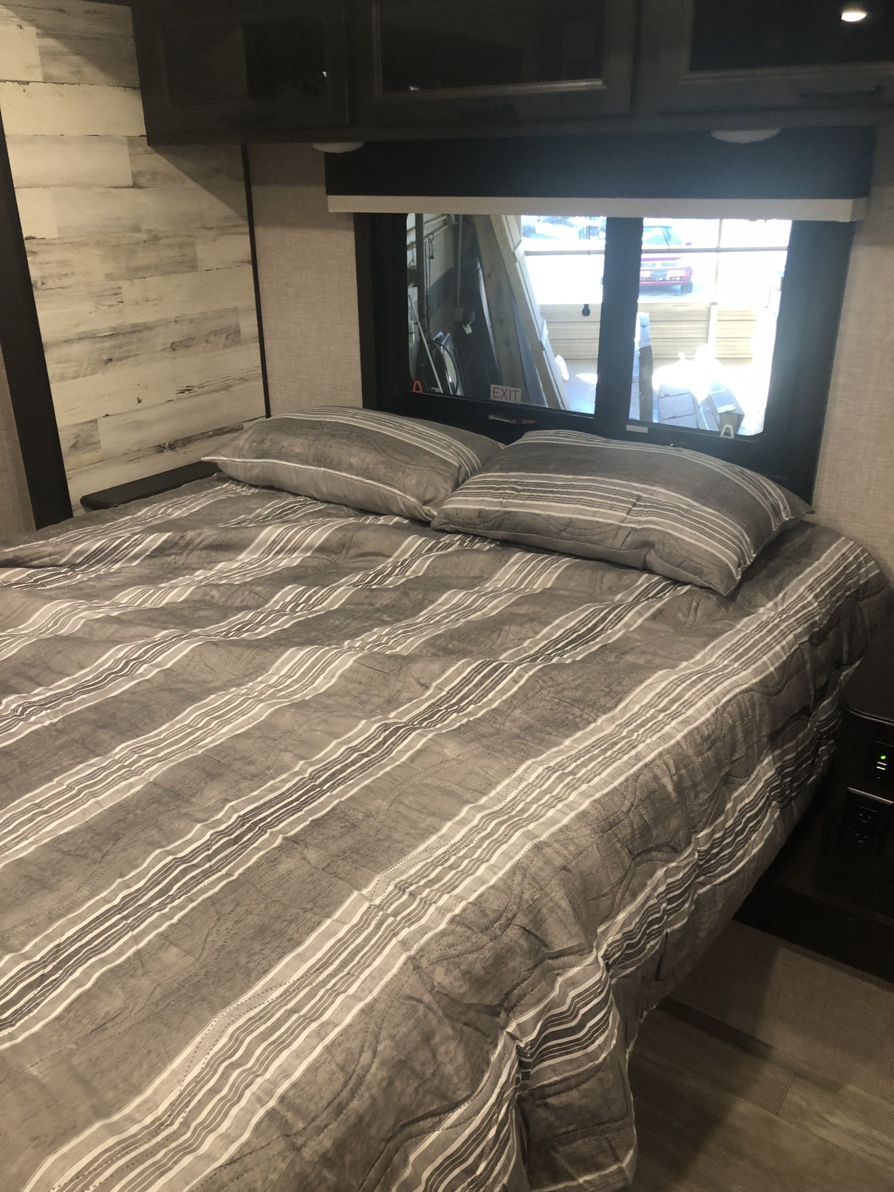 Comfortable RV rental bed with gray striped bedding, a bright window view, and light wood walls.. Jayco White Hawk 2023