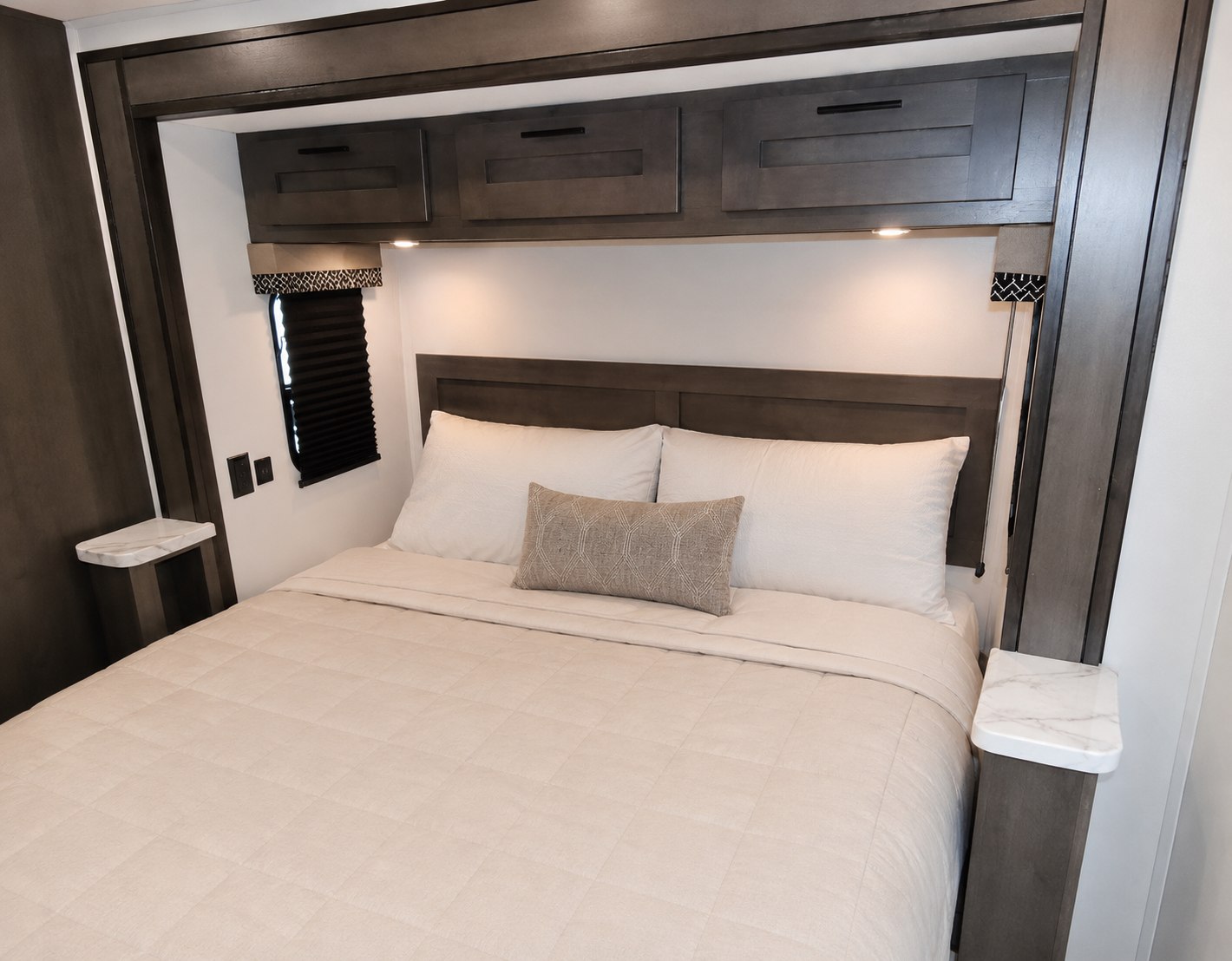 Modern RV rental bedroom featuring a queen bed with white bedding, overhead storage, and convenient side ledges. A cozy retreat.. Forest River FR3 2022