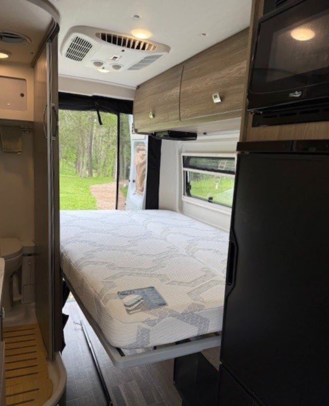 Comfortable RV rental interior featuring a fold-down bed, compact bathroom, and kitchen appliances. Perfect for travel.. Winnebago Travato 2023