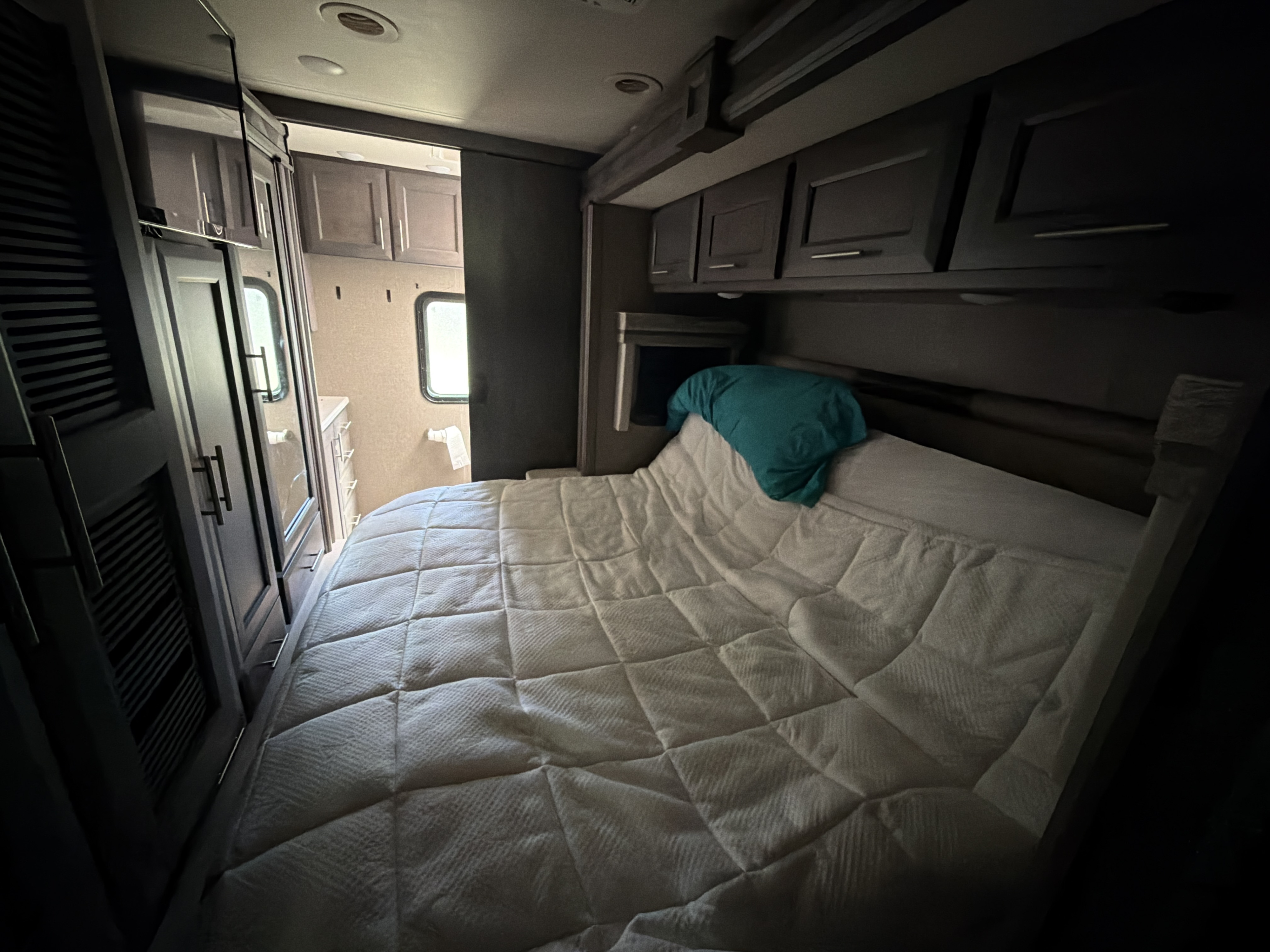 Interior of a compact RV rental bedroom. A bed with a white quilted comforter is central, with overhead cabinets and a closet to the left.. Thor Miramar 2022