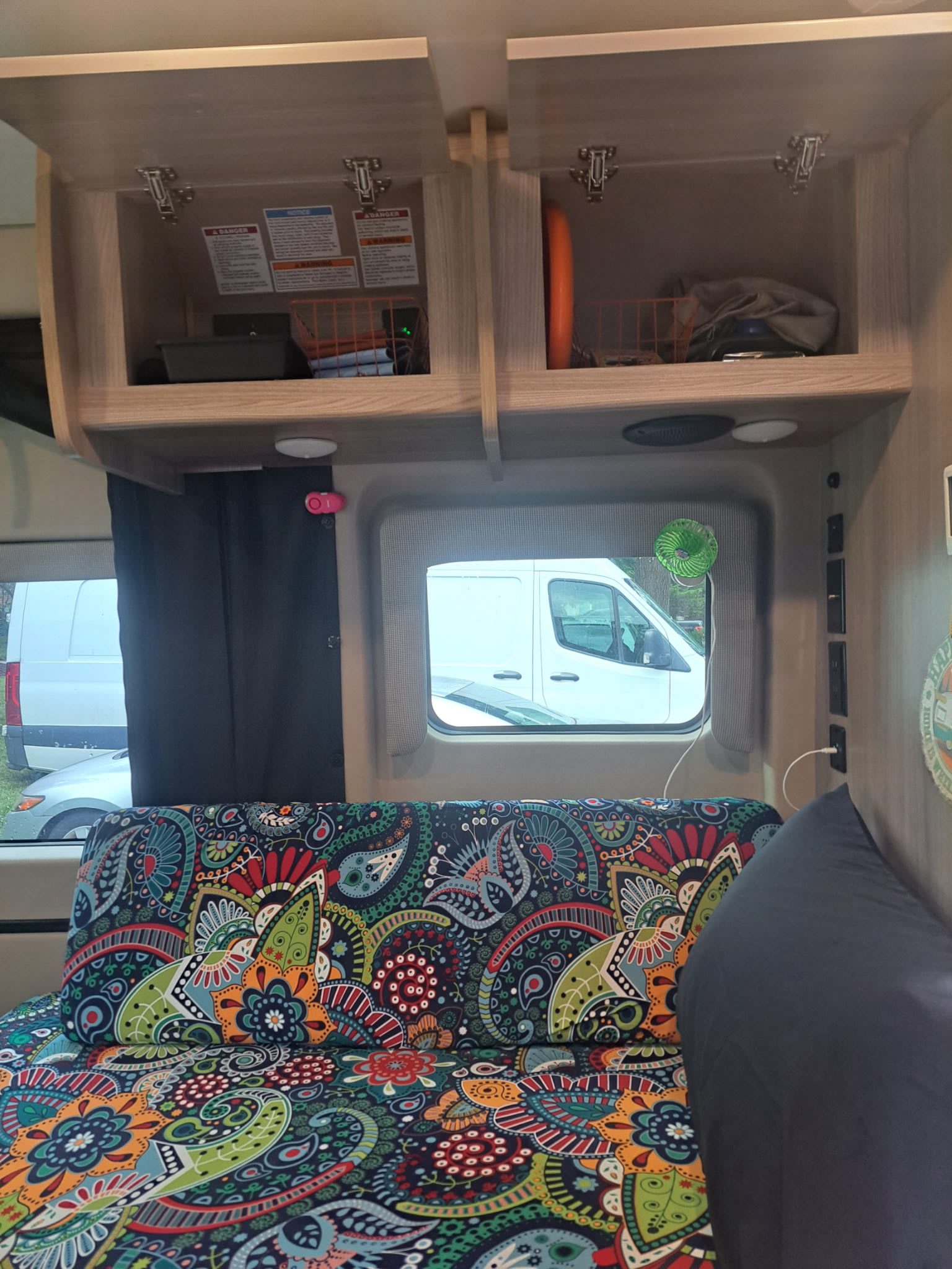 RV rental interior: open cabinets, a vibrant paisley couch, window with a fan, and wall outlets.. Thor Scope 2024