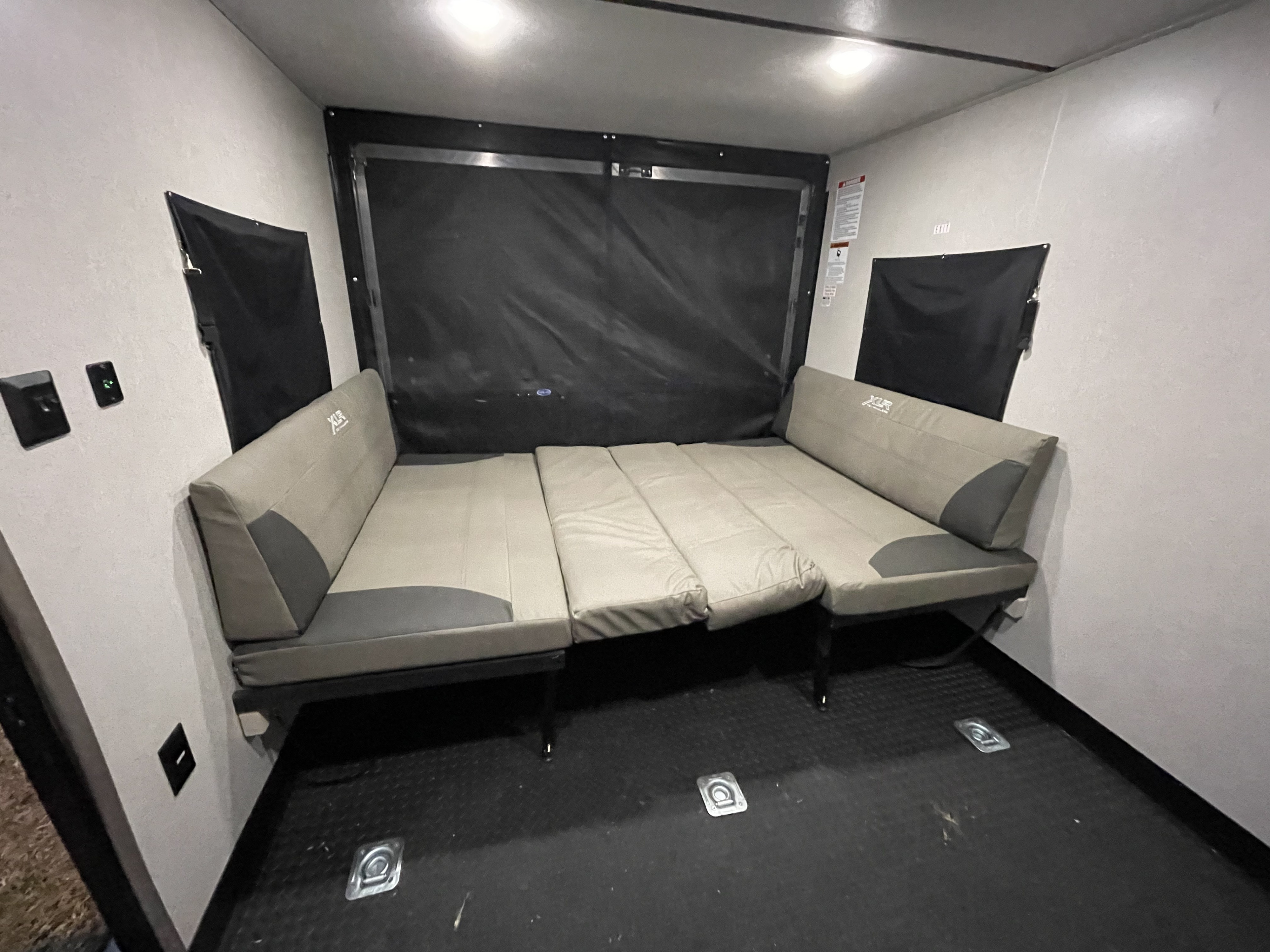 This RV rental's cargo area features modular bench seats converted into a bed, with a black floor, tie-downs, and wall outlets.. Forest River XLR Micro Boost Toy Hauler 2021
