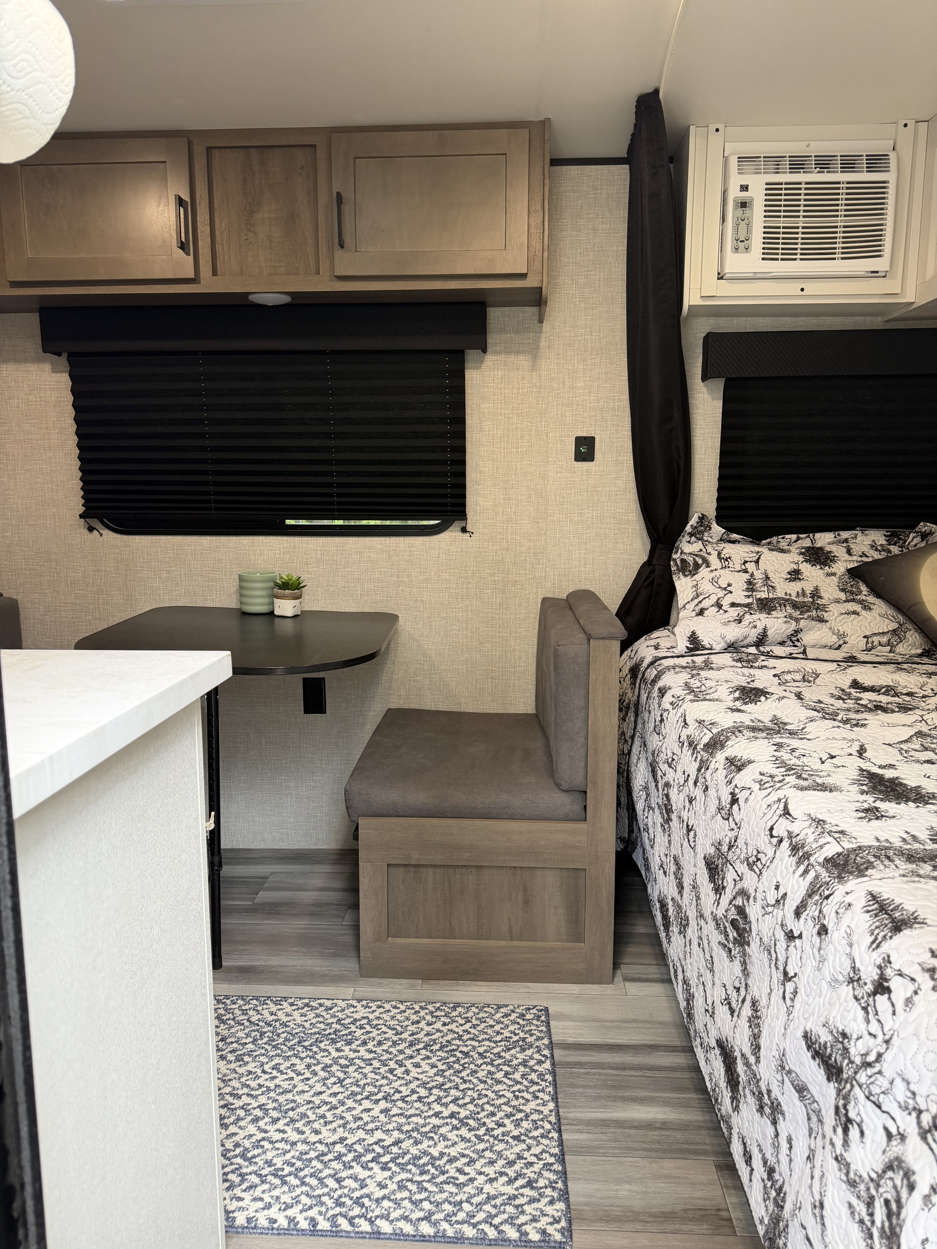 Cozy RV rental interior with dinette, bed featuring nature-themed bedding, storage cabinets, and AC unit.. Jayco Jay Flight SLX 2024