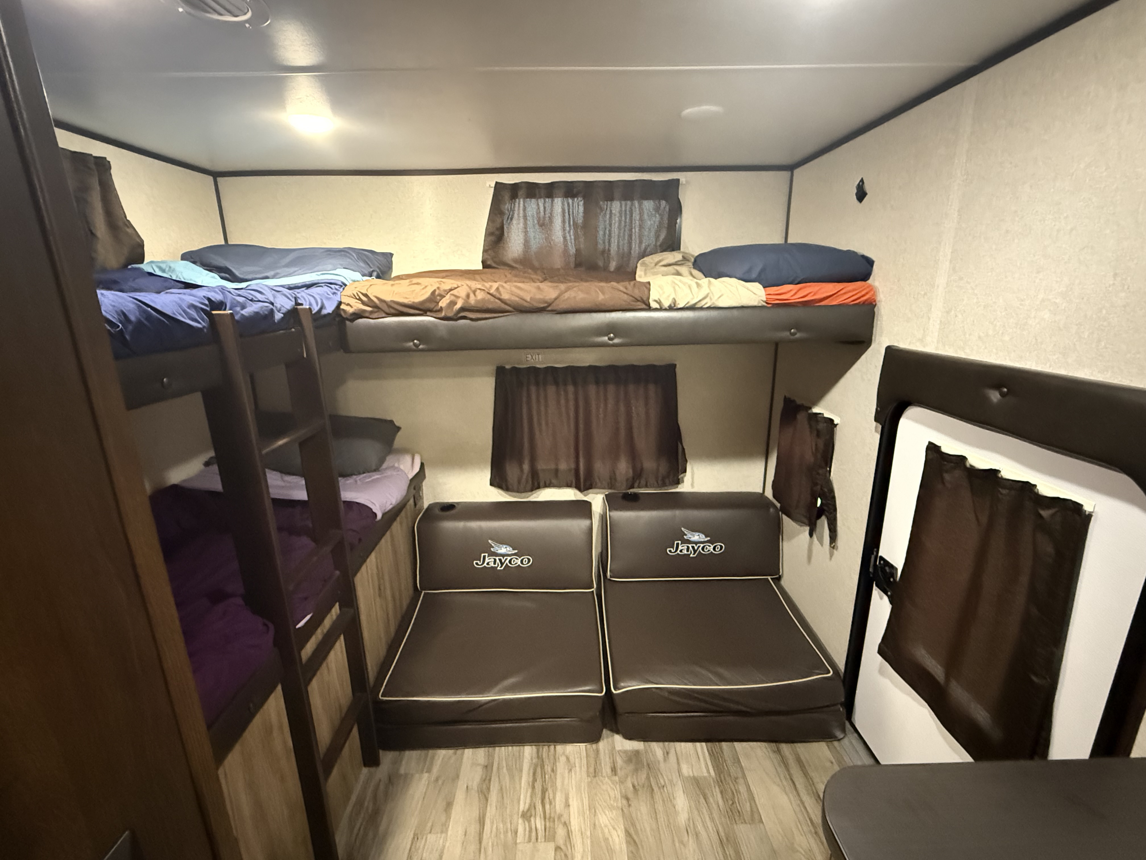 RV rental interior featuring bunk beds, lounge seating with Jayco logo, and brown curtains, providing sleeping and seating space.. Jayco Jay Feather 2019