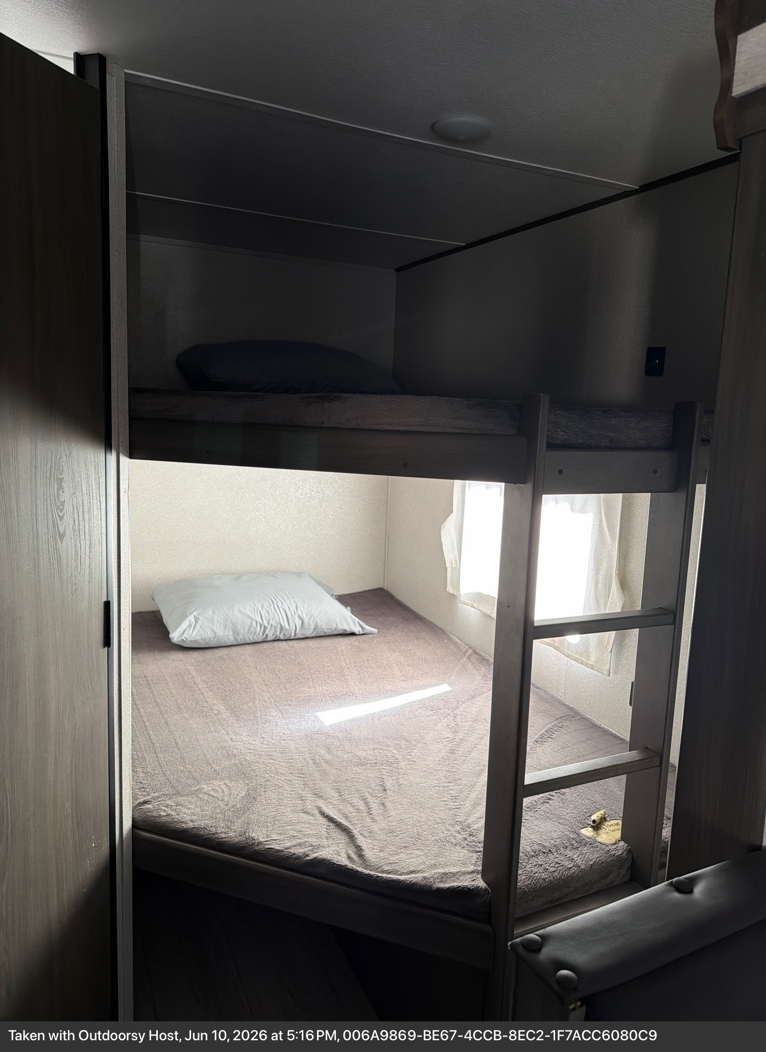 Interior of an RV rental featuring comfortable bunk beds with soft bedding and natural light from a window.. Forest River Shasta 2021