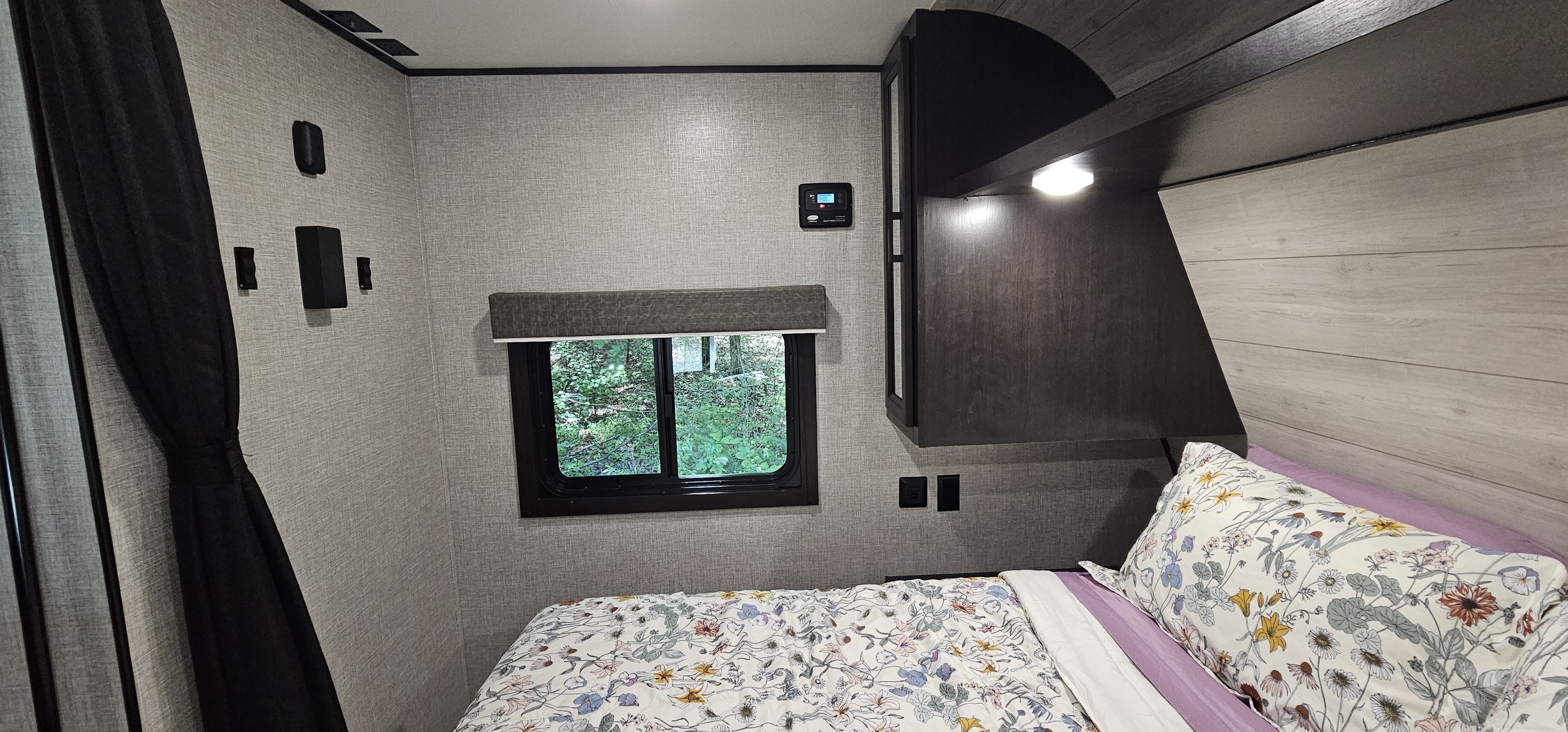Cozy RV rental bedroom featuring floral bedding, a window with a lush tree view, and wall-mounted controls.. Jayco Jay Flight SLX 2022