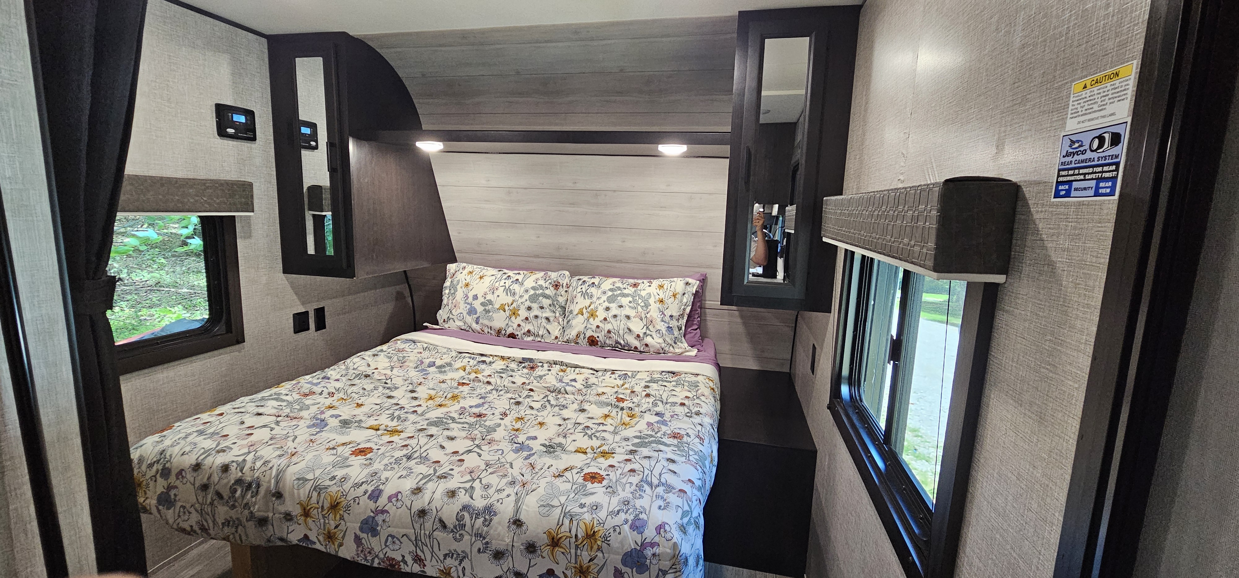 Relax in this RV rental's bedroom, featuring a floral bed, bright windows, and convenient overhead storage.. Jayco Jay Flight SLX 2022