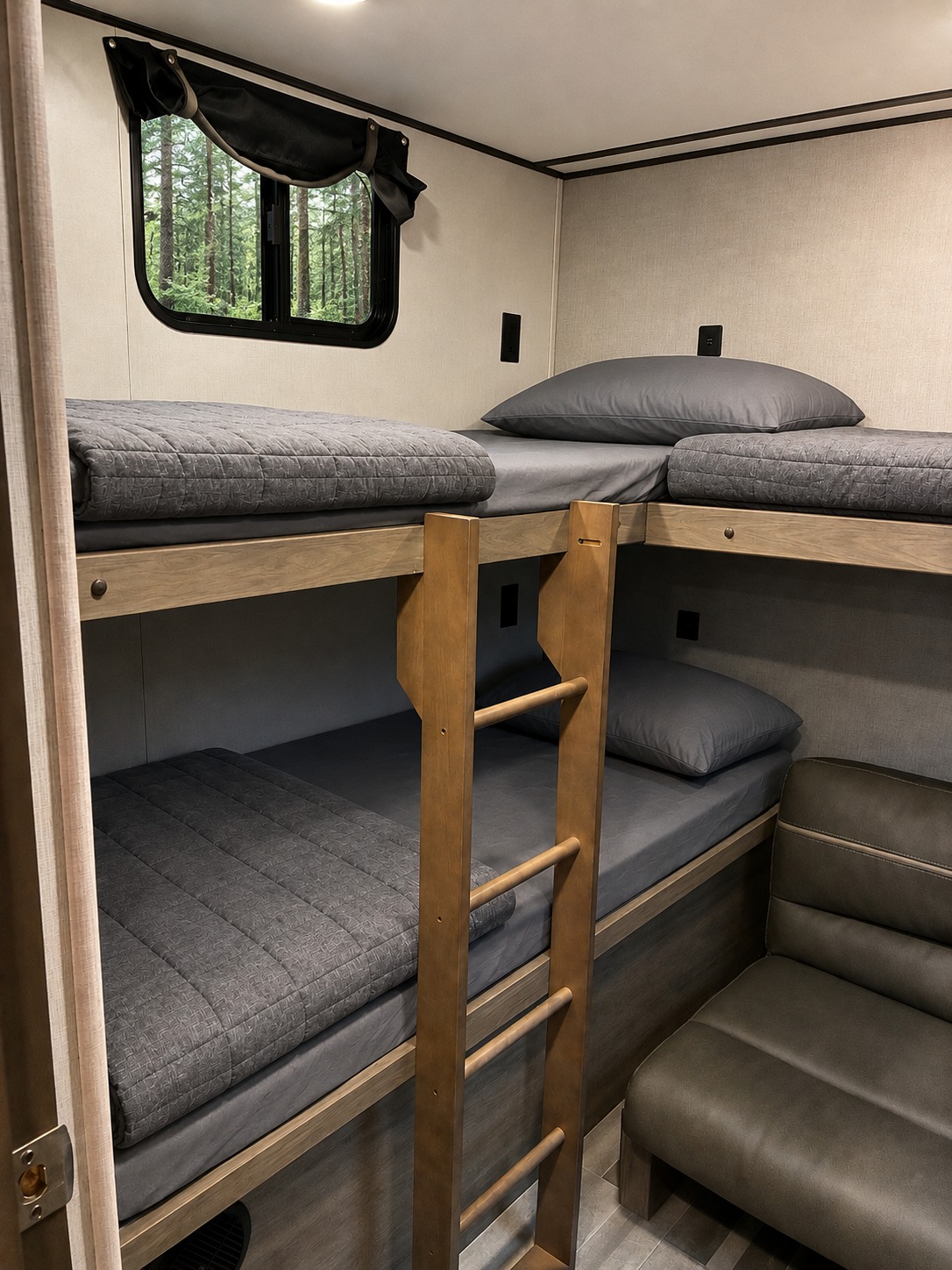 Cozy RV rental bedroom with two sets of bunk beds, grey bedding, a wooden ladder, a window overlooking a forest, and a small sofa.. Crossroads RV Zinger 2021