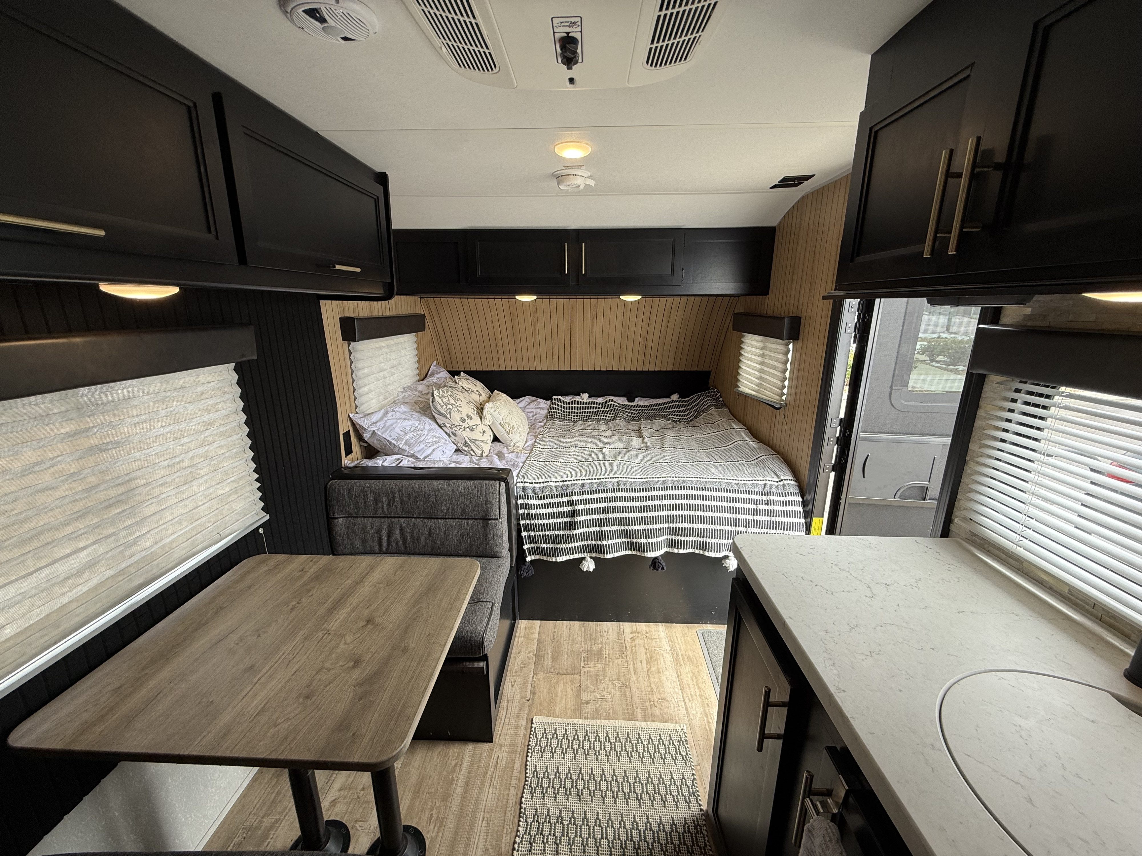 Stylish RV rental interior with a cozy bed, dinette, and kitchenette. Features sleek black cabinets and warm wood paneling.. Forest River Cherokee Wolf Pup 2021