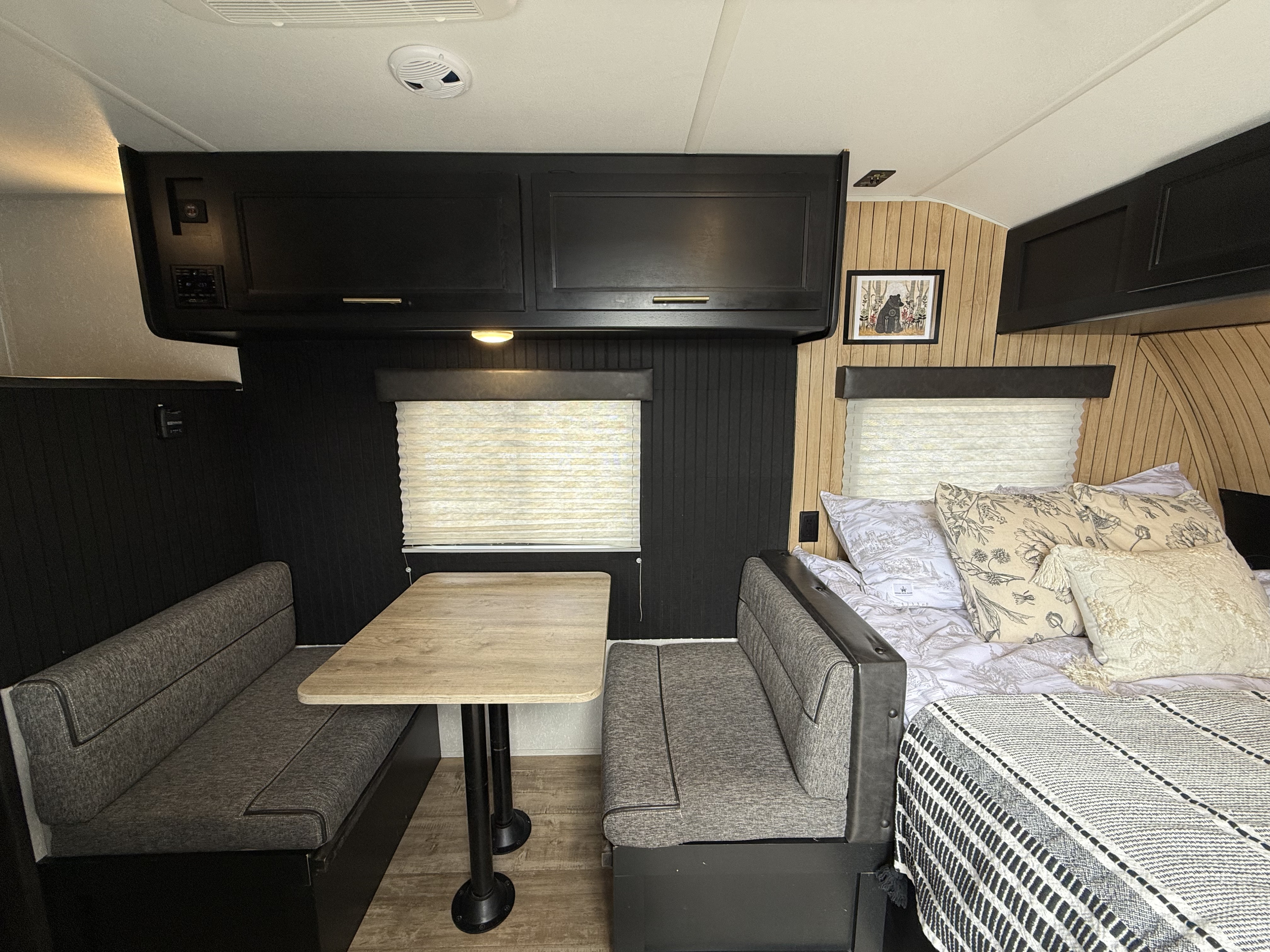 Modern RV rental interior: dinette, bed, sleek black cabinets, and mixed-material walls with window blinds.. Forest River Cherokee Wolf Pup 2021
