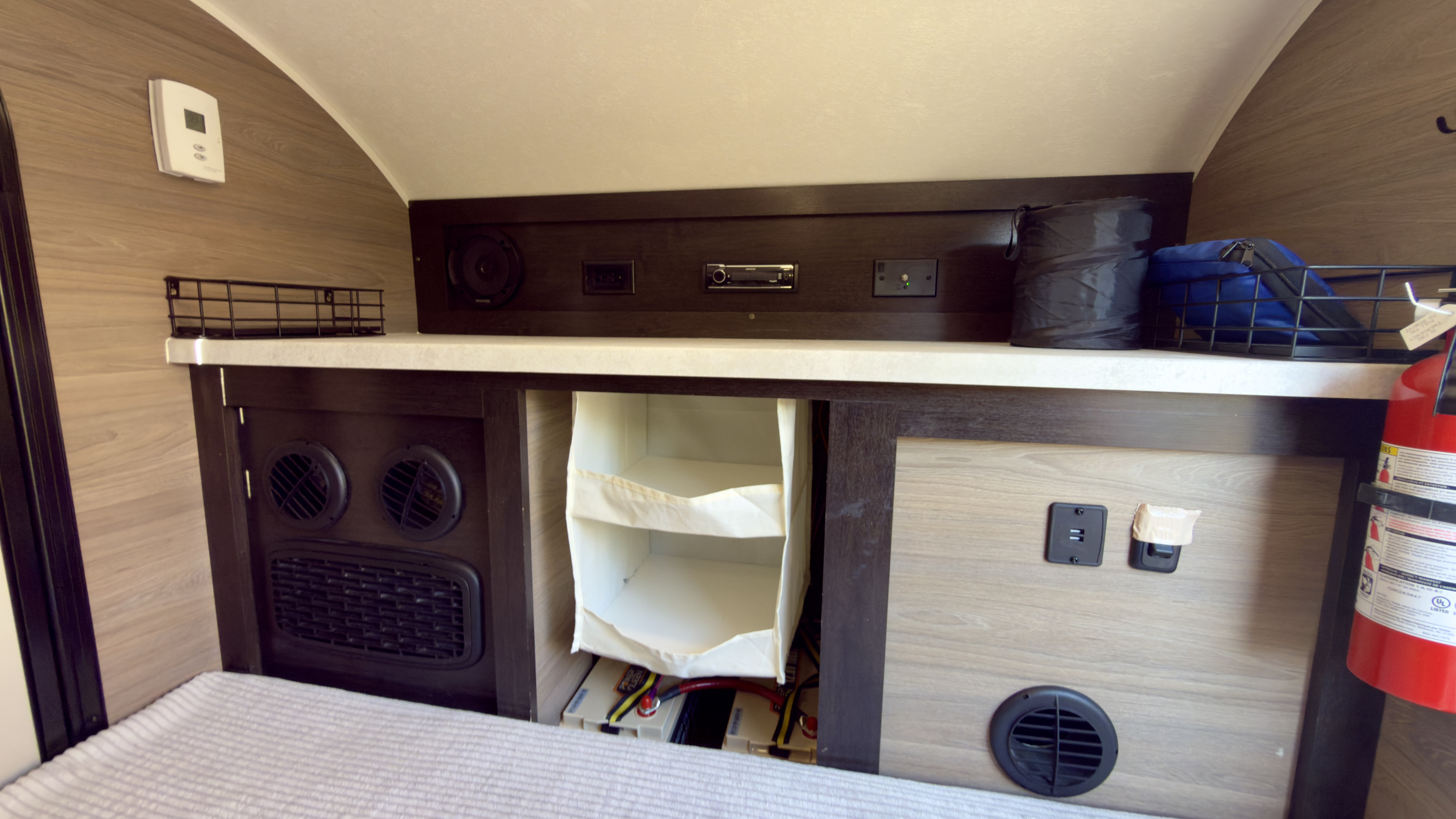 View of an RV rental's bed area, featuring integrated storage, a stereo, climate control, and a fire extinguisher for safety.. Braxton Creek Bushwhacker 2024
