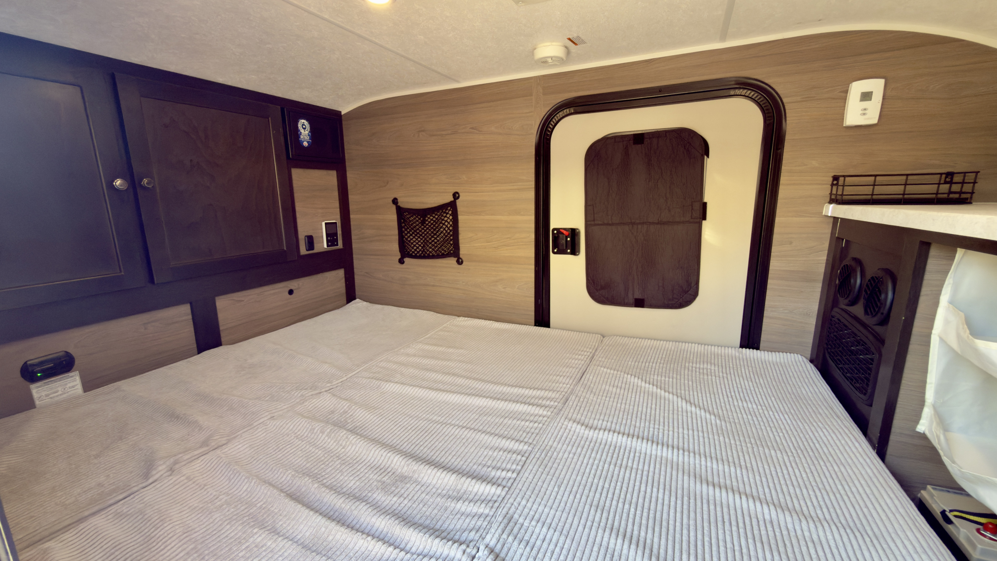 Spacious bed and dark wood cabinets in a clean rv rental interior, with a side door and control panels for comfort.. Braxton Creek Bushwhacker 2024
