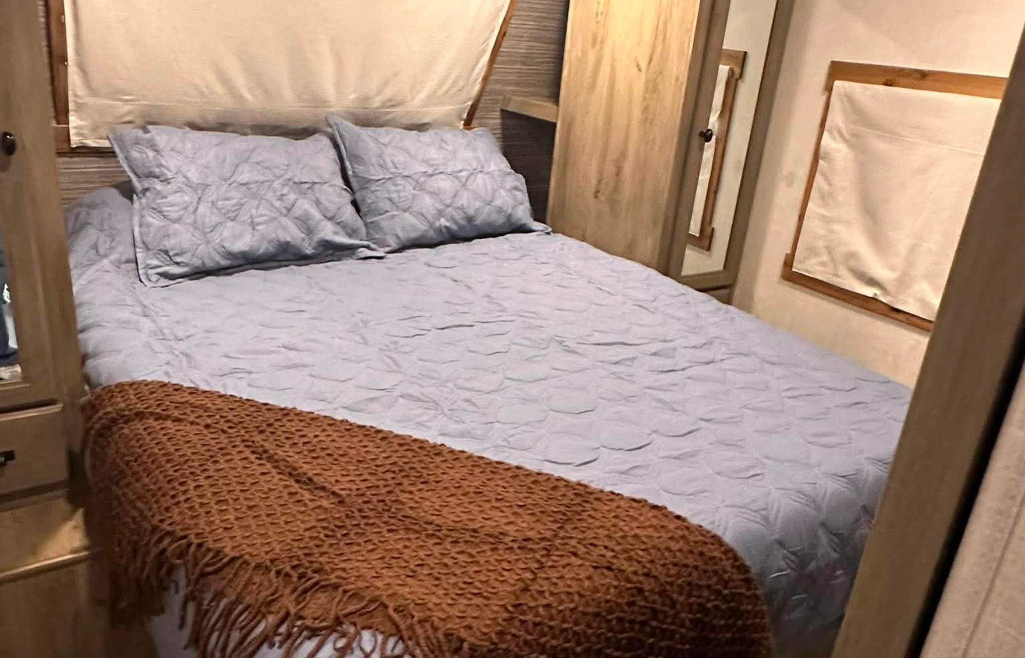 Cozy RV rental bedroom with blue quilted bedding, a rustic throw, and warm wood accents, perfect for relaxing.. Forest River Surveyor Legend 2021