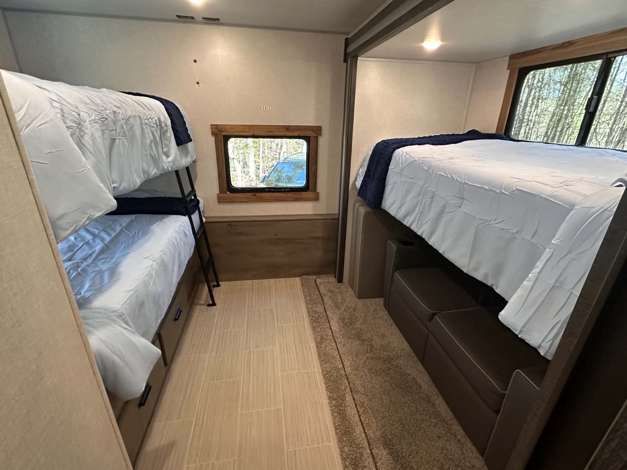 Interior of an RV rental: bunk beds on left, single bunk over seating on right, window, and mixed flooring.. Forest River Surveyor Legend 2021