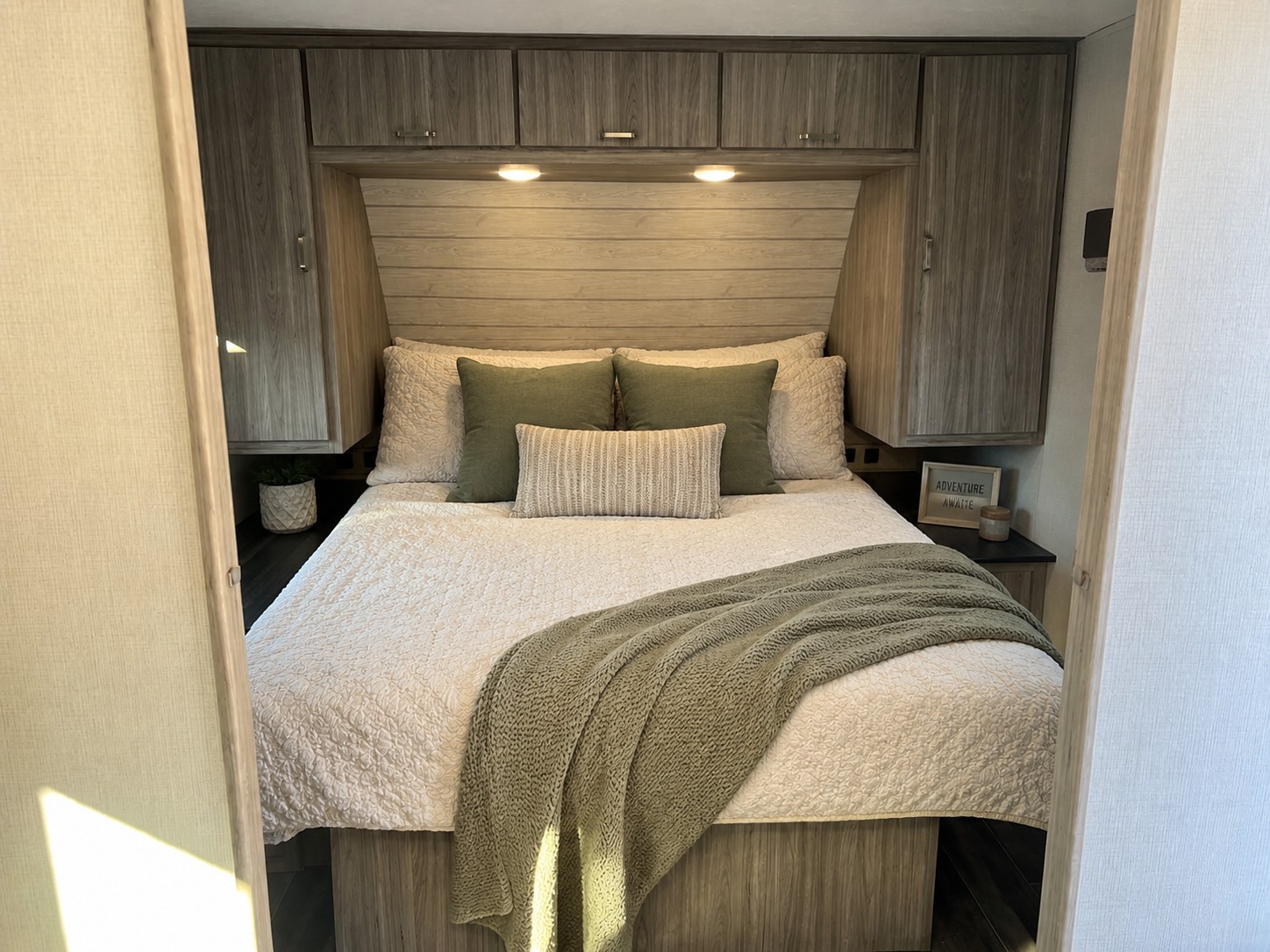Cozy RV rental bedroom featuring a comfy bed with green and cream bedding, ample storage, and warm lighting.. Keystone RV Passport SL 2022