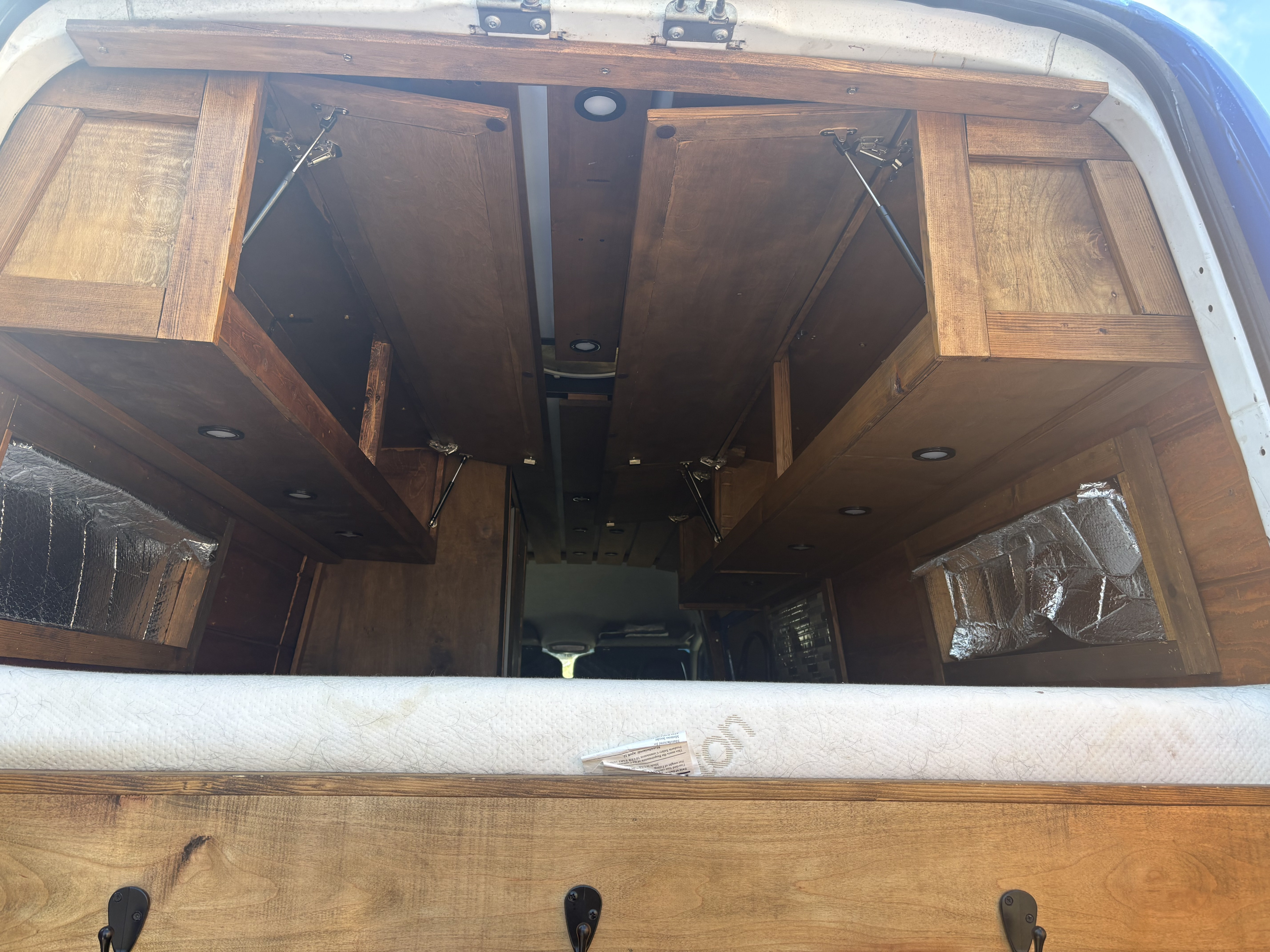 Inside an RV rental: Wooden interior with open overhead cabinets, recessed lights, and a bed in a camper van.. Dodge Sprinter Van 2008
