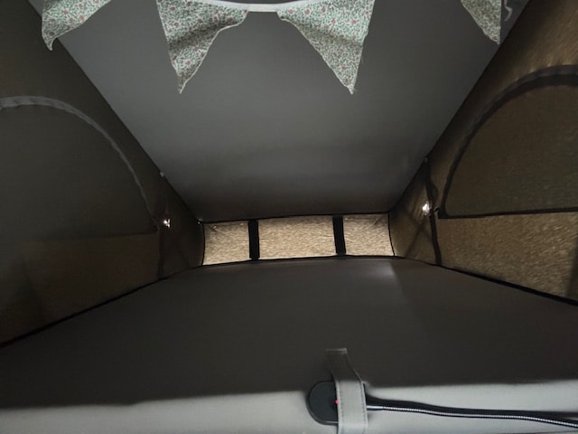 Inside an RV rental pop-top: a cozy sleeping loft with light-filtering windows, decorative bunting, and secure straps.. Volkswagen California 2015