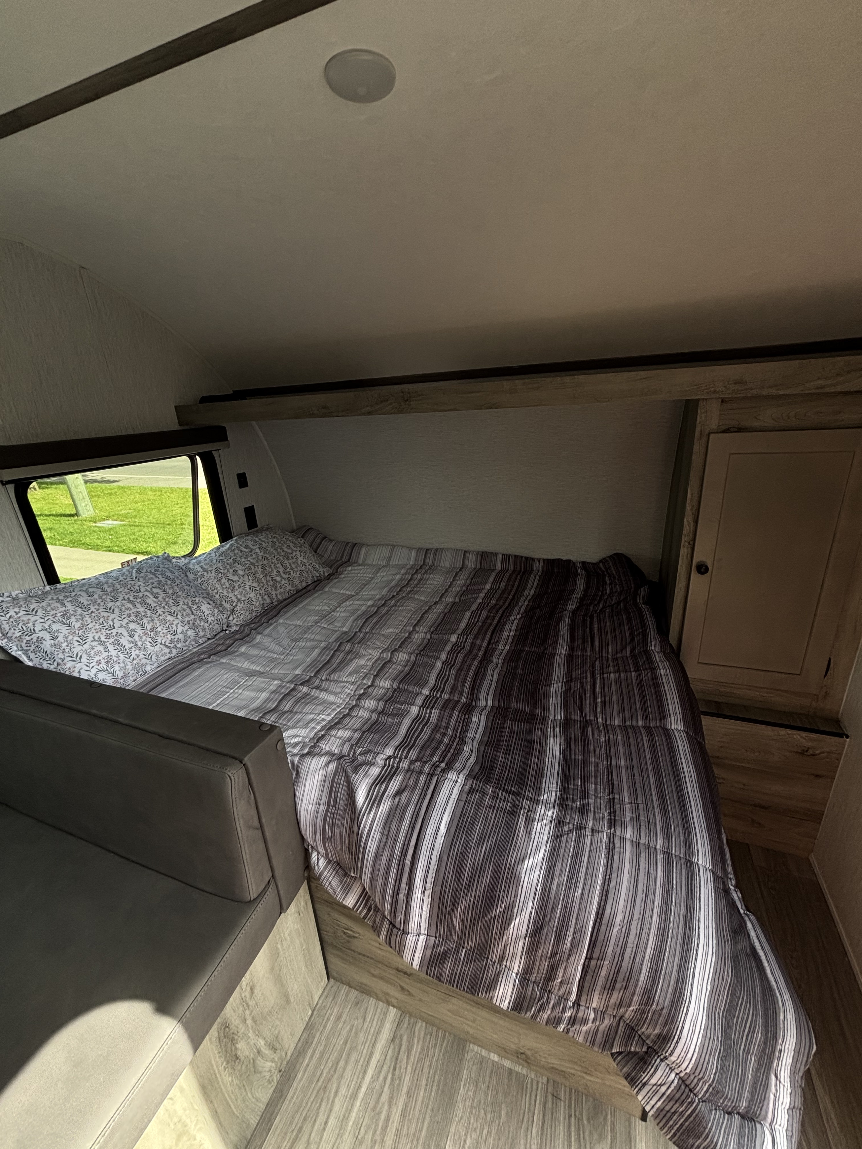 Cozy RV rental bedroom with a striped comforter, floral pillows, and a window view, offering a comfortable sleeping area.. Sunset Park RV Sun Lite LTD 2026