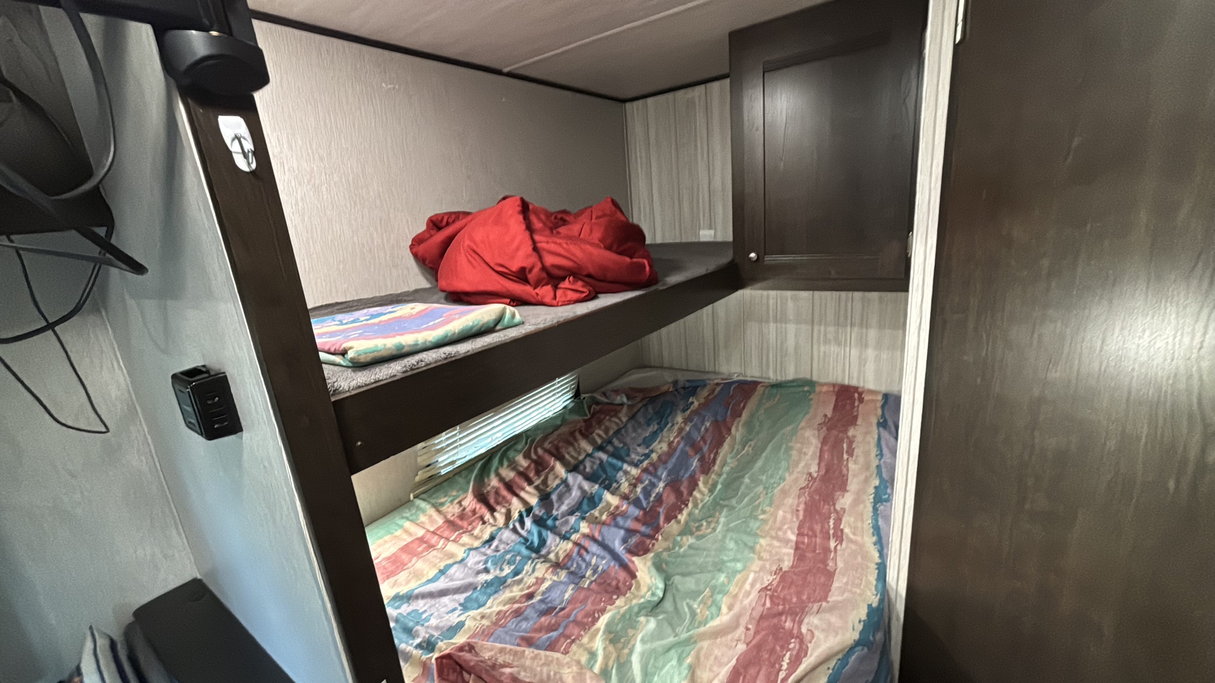 Inside an RV rental: view of bunk beds with colorful blankets, a cabinet, window, and wall-mounted charger.. Heartland RVs Pioneer 2021