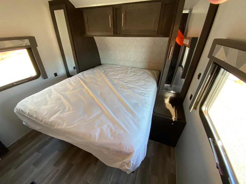 RV rental bedroom featuring a bed with protective plastic, overhead cabinets, and bright windows for your next adventure.. Forest River Salem 2020