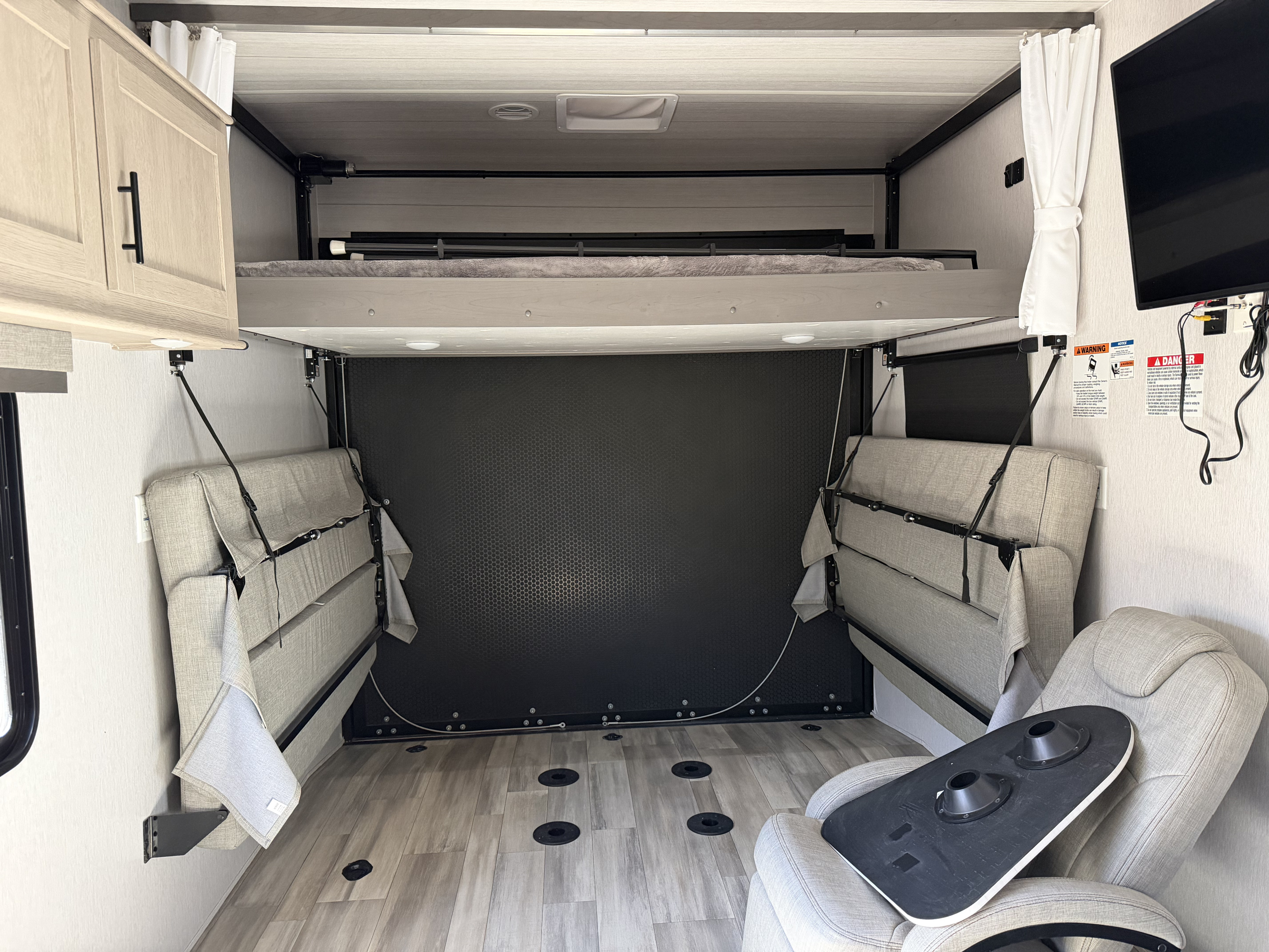 Inside an RV rental, a versatile toy hauler space features a raised bunk bed, fold-down sofas, and floor tie-downs.. Forest River Stealth 2023