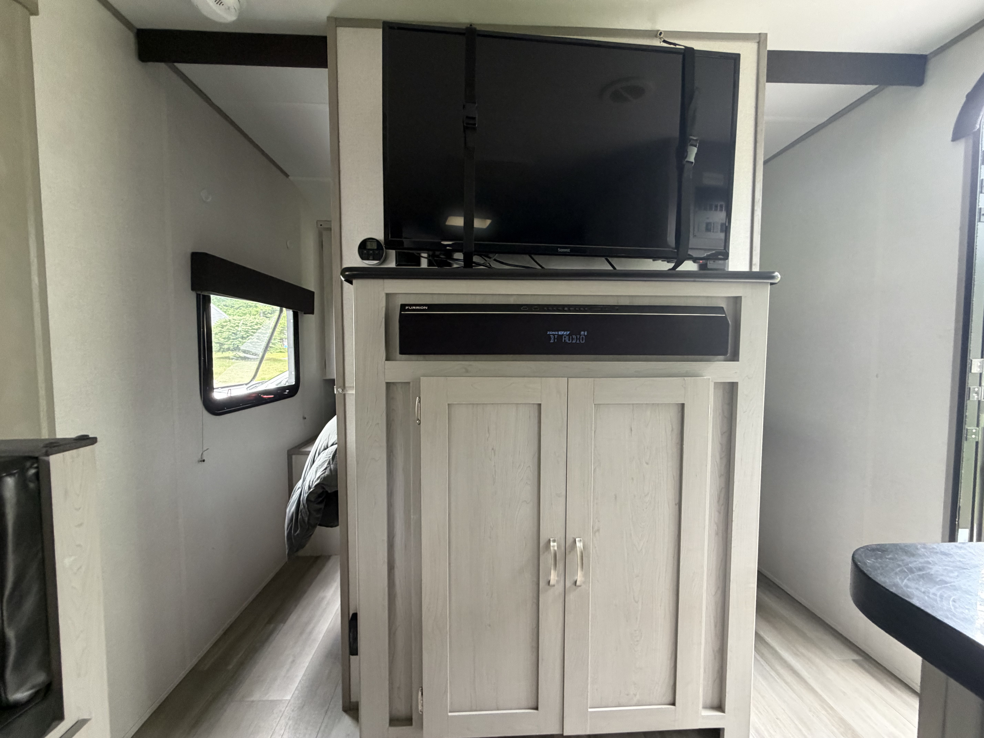 RV rental interior: TV, soundbar, and cabinets in a compact living area, leading to a bedroom with a window.. Forest River Tracer 2022