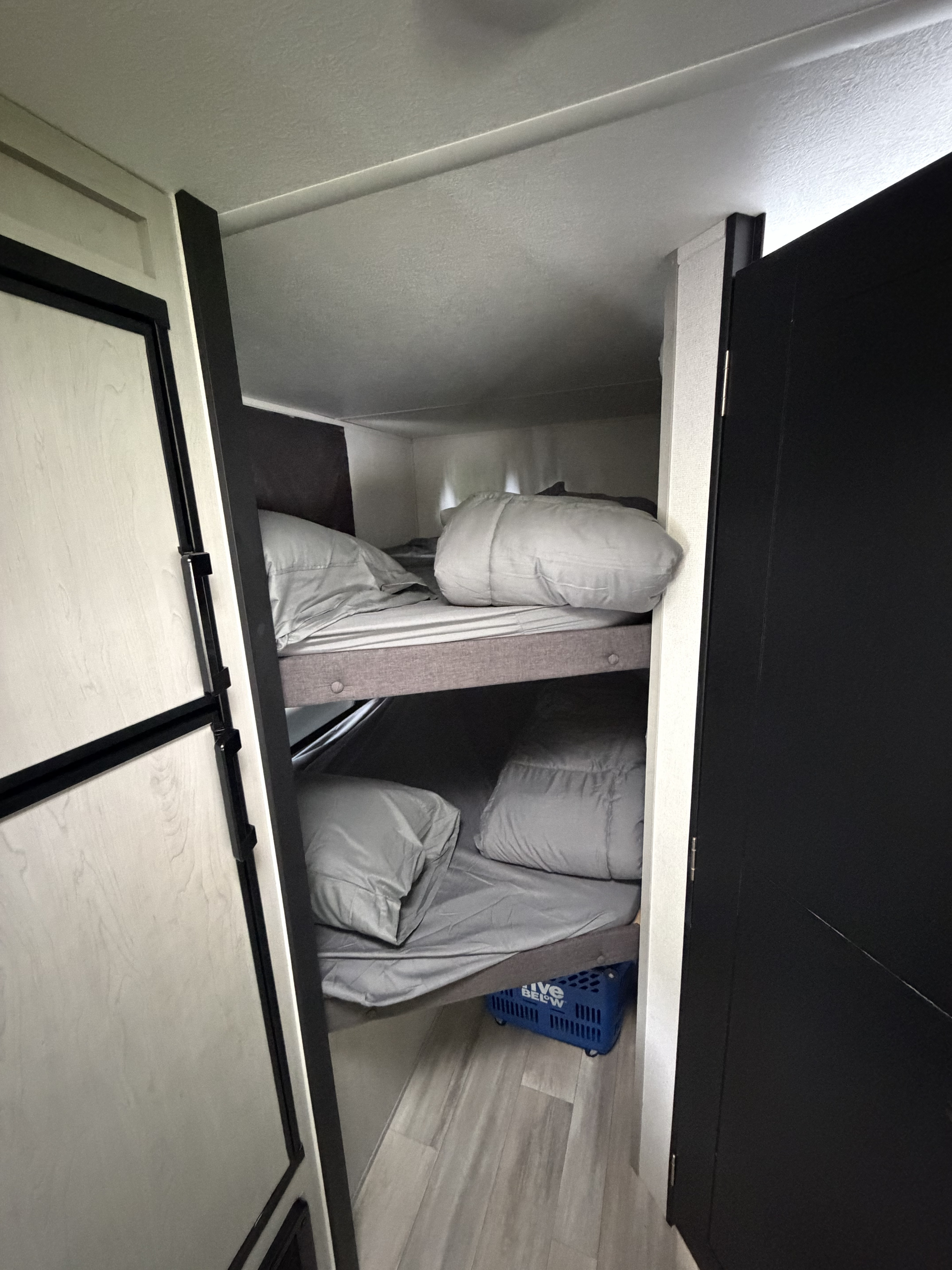 Inside an RV rental: cozy bunk beds with gray bedding and pillows, offering compact sleeping space. A blue basket sits below.. Forest River Tracer 2022