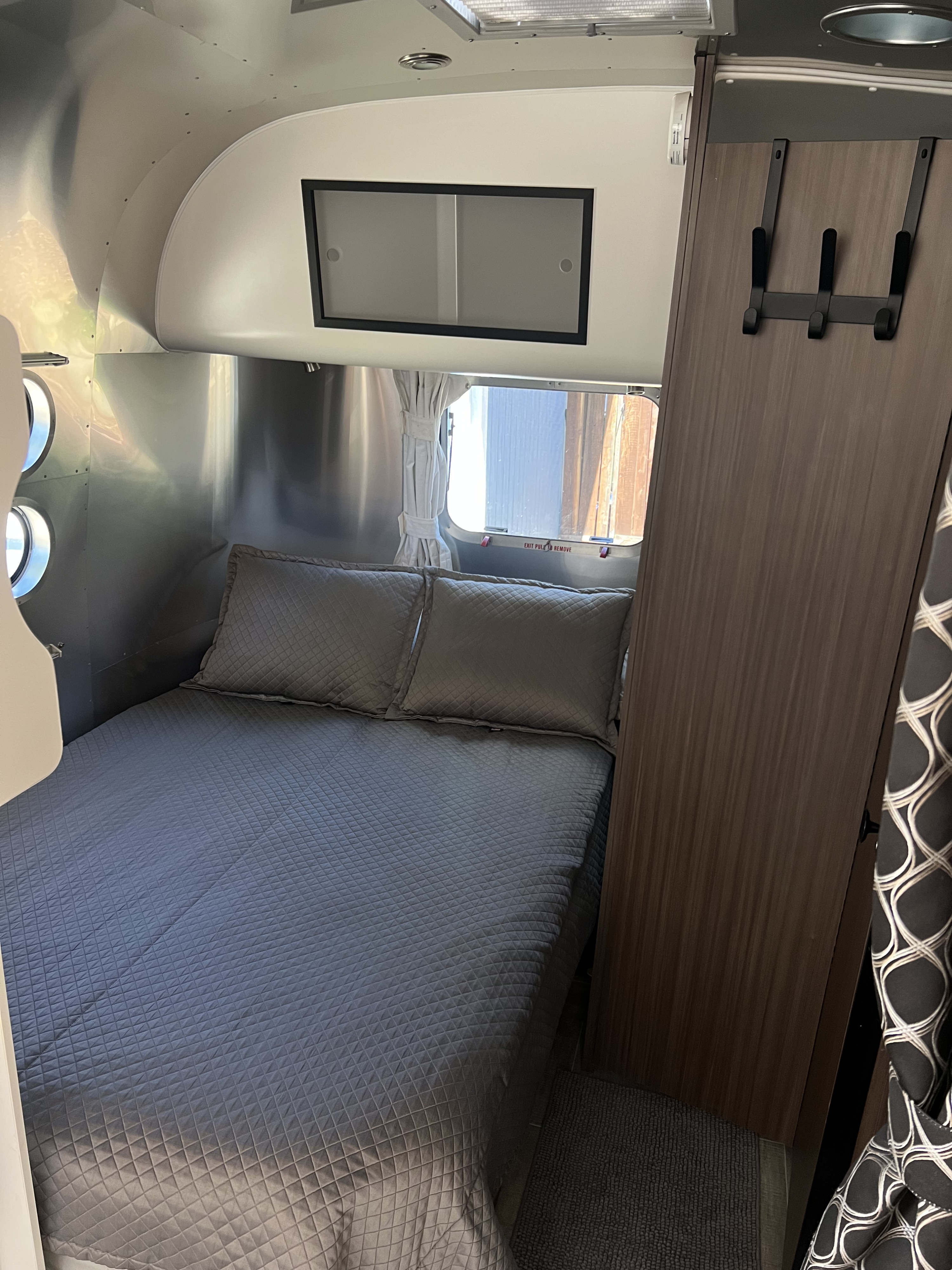 RV rental bedroom: a compact space with quilted gray bed, metallic walls, overhead cabinet, and wardrobe with hooks.. Airstream Caravel 2020