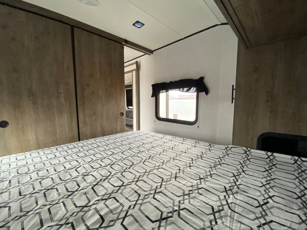 Interior of an RV rental bedroom featuring a geometric patterned bed, wood-look sliding closet doors, and a window with a water view.. Heartland RVs Pioneer 2021