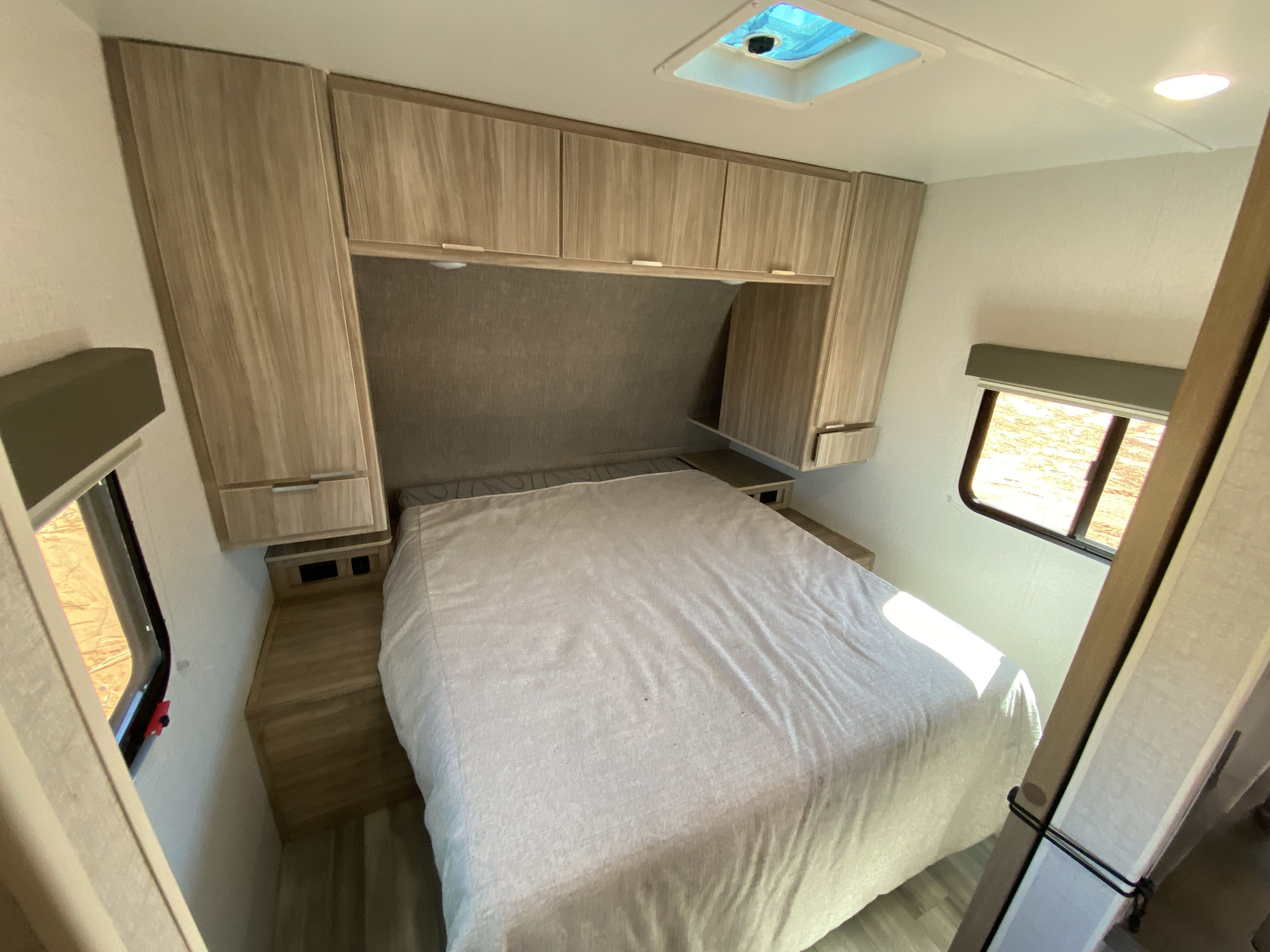 Cozy RV rental bedroom featuring light wood cabinets, a comfortable bed, and windows for natural light.. Winnebago Minnie Winnie 2022