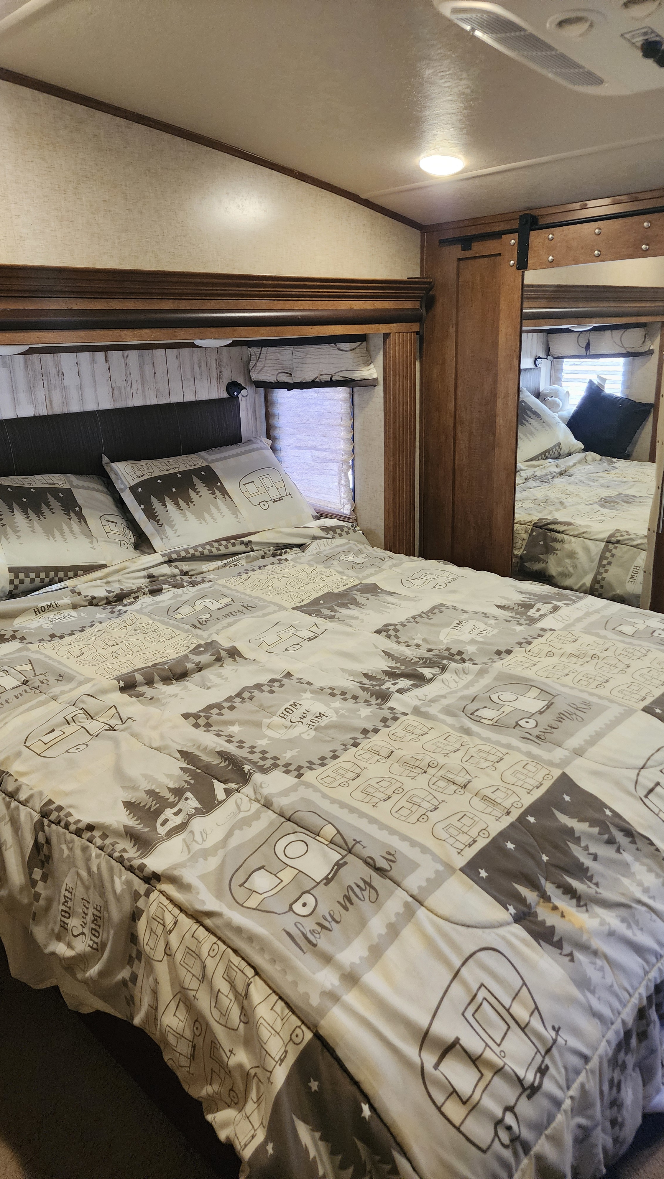 This cozy RV rental bedroom features a bed with a comforter showcasing vintage campers, trees, and "Home Sweet Home" text.. Forest River Sabre 2018