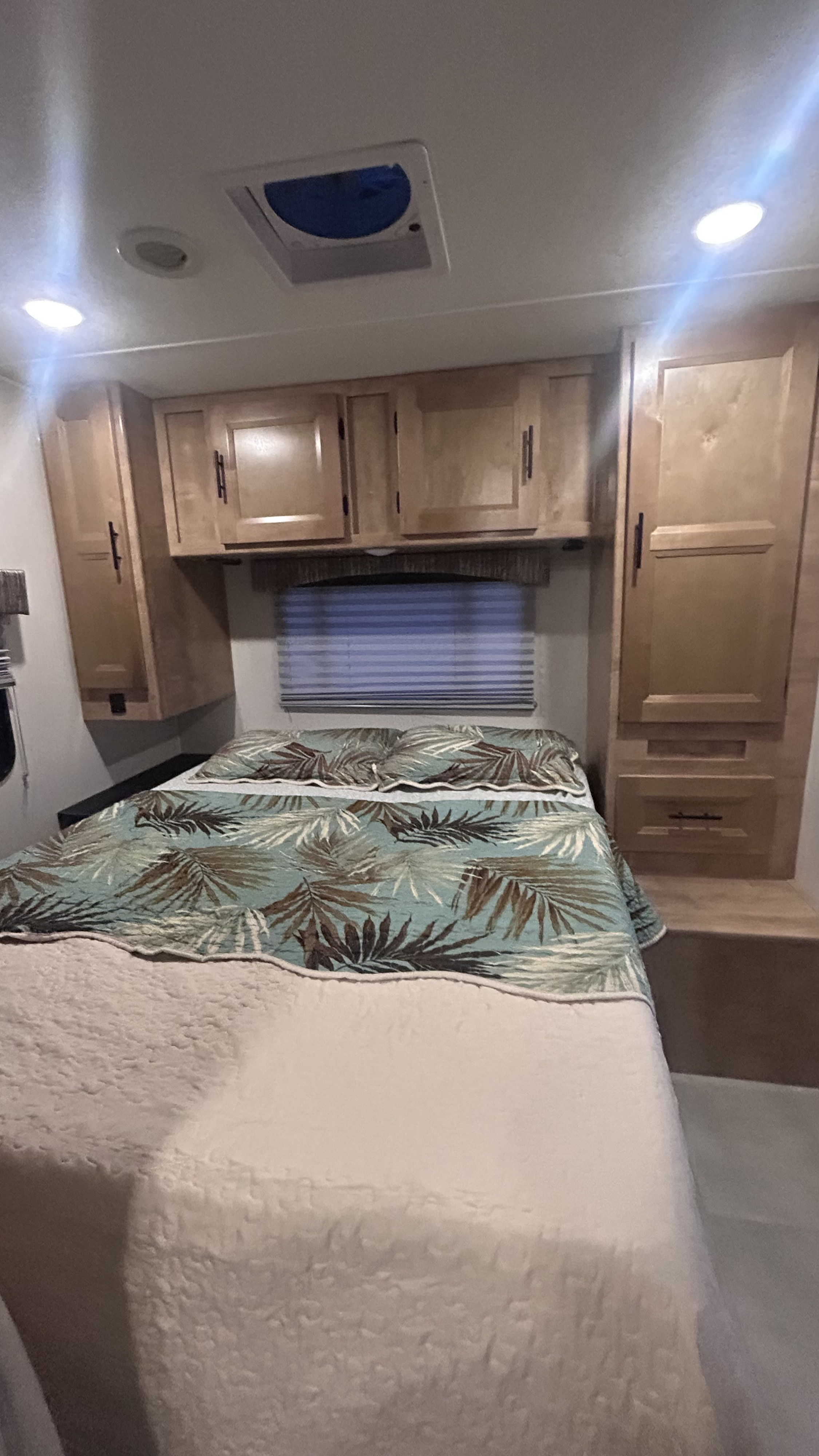 RV rental bedroom featuring tropical bedding, wood cabinets, ceiling vent, and lighting for comfortable travel.. Forest River Coachmen Leprechaun 2022