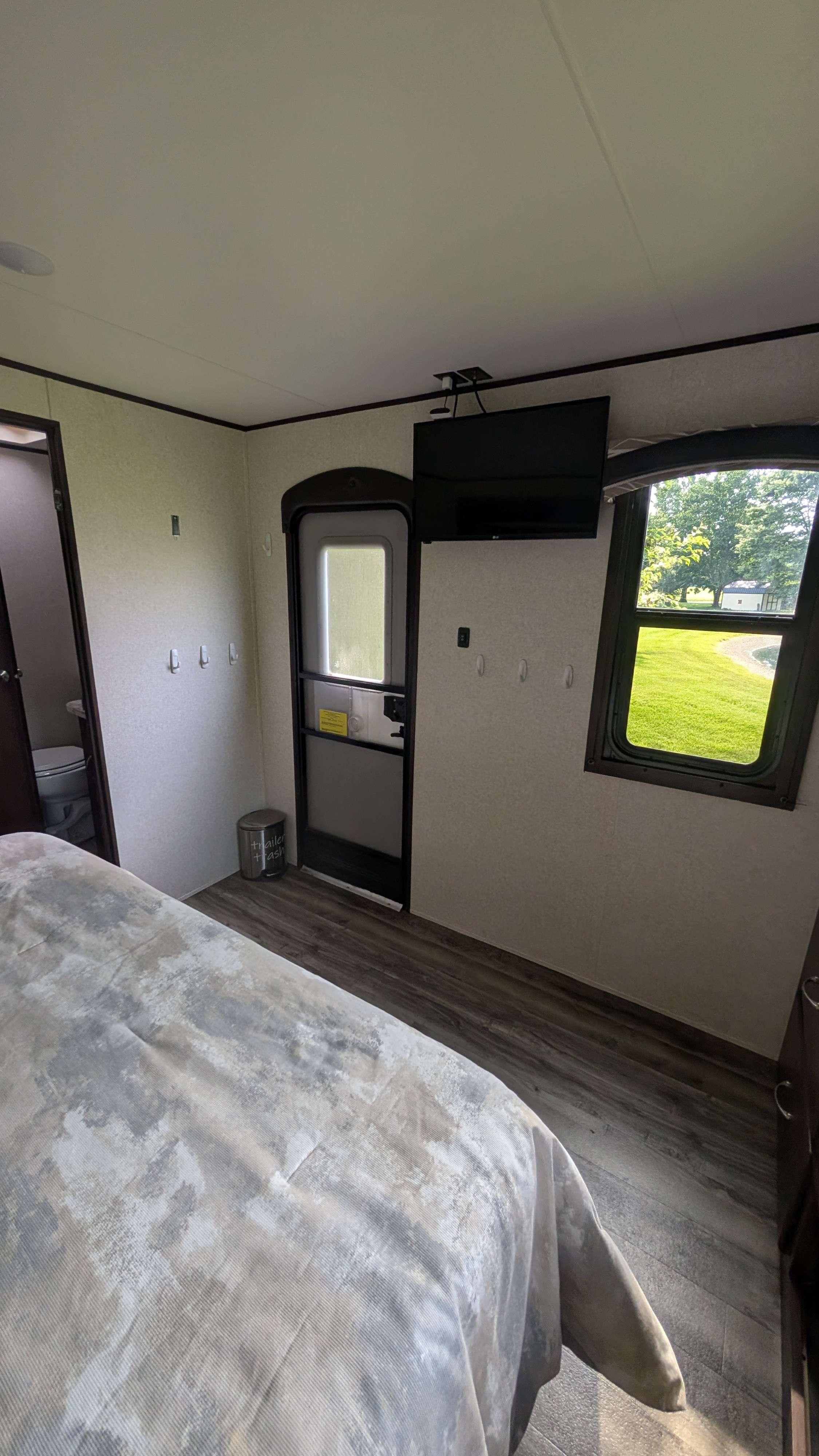 Inside an RV rental: a cozy bedroom with a bed, TV, bathroom access, and a view of nature.. Jayco Jay Flight 2017