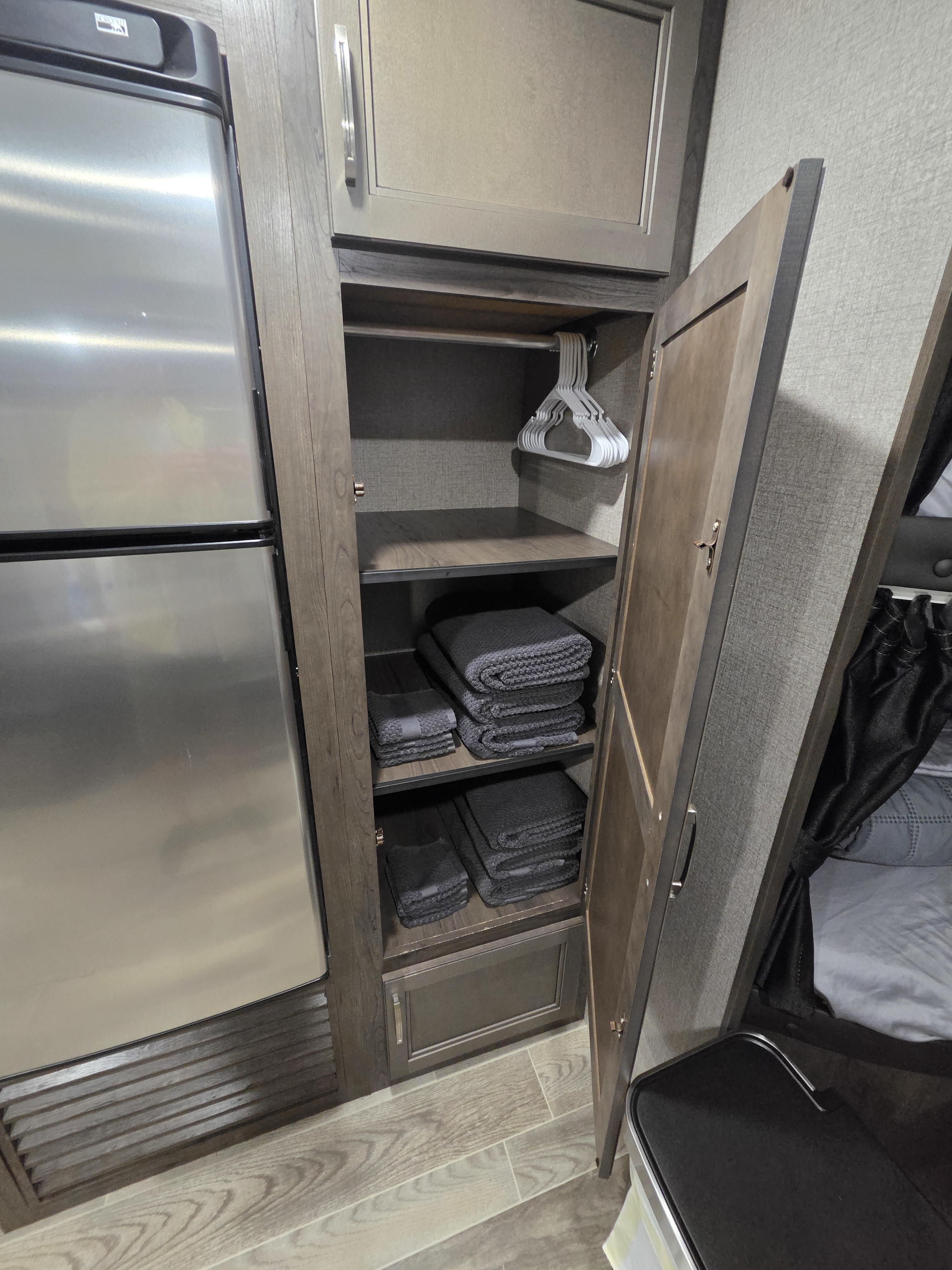 Well-organized RV rental interior: stainless fridge, open wardrobe with hanging space, neatly folded towels, and nearby sleeping area.. Jayco Jay Flight SLX 2021