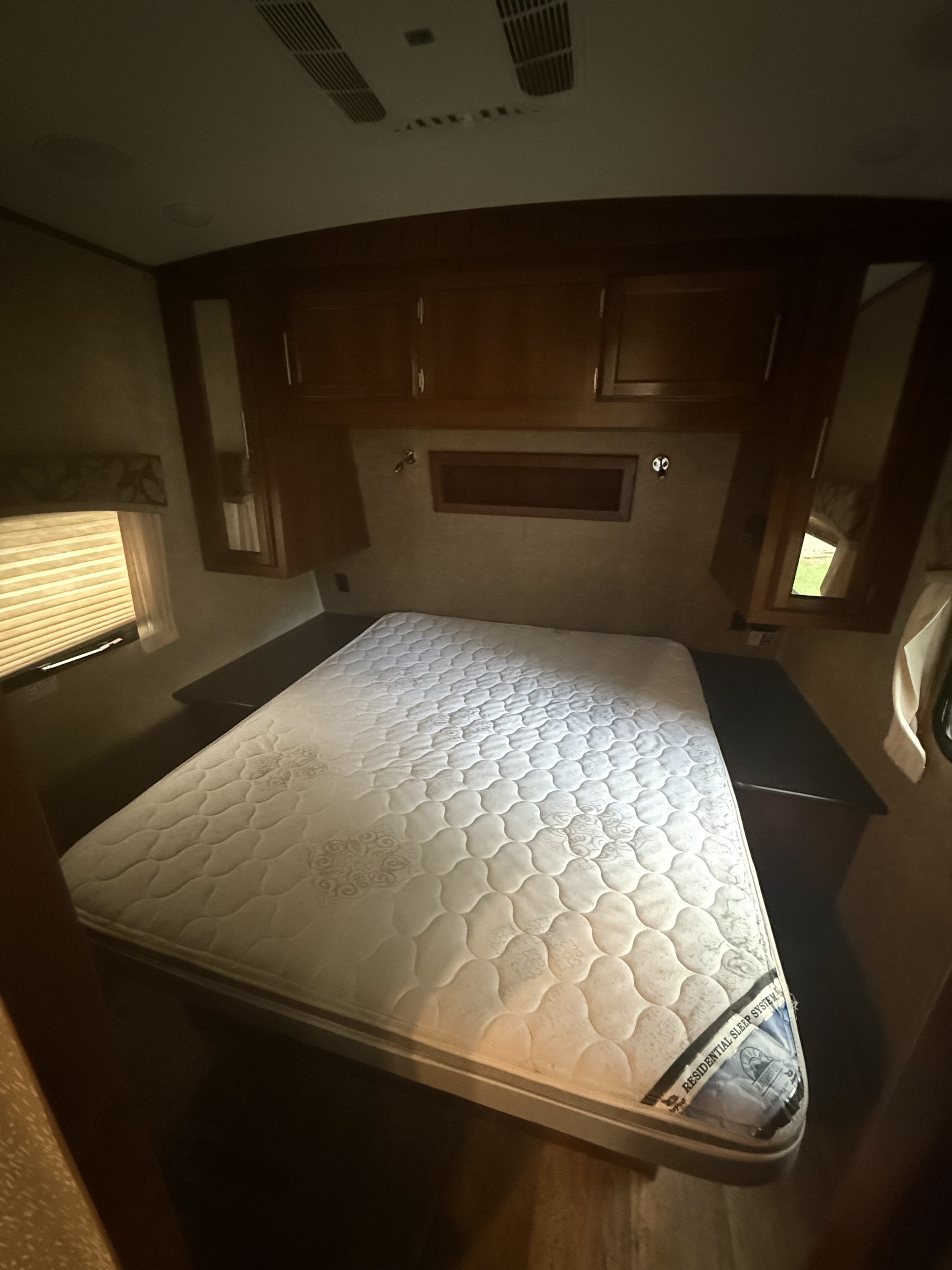 A compact RV rental bedroom featuring a quilted mattress, wooden cabinets, window with blinds, and ceiling vents.. Jayco Eagle 2016