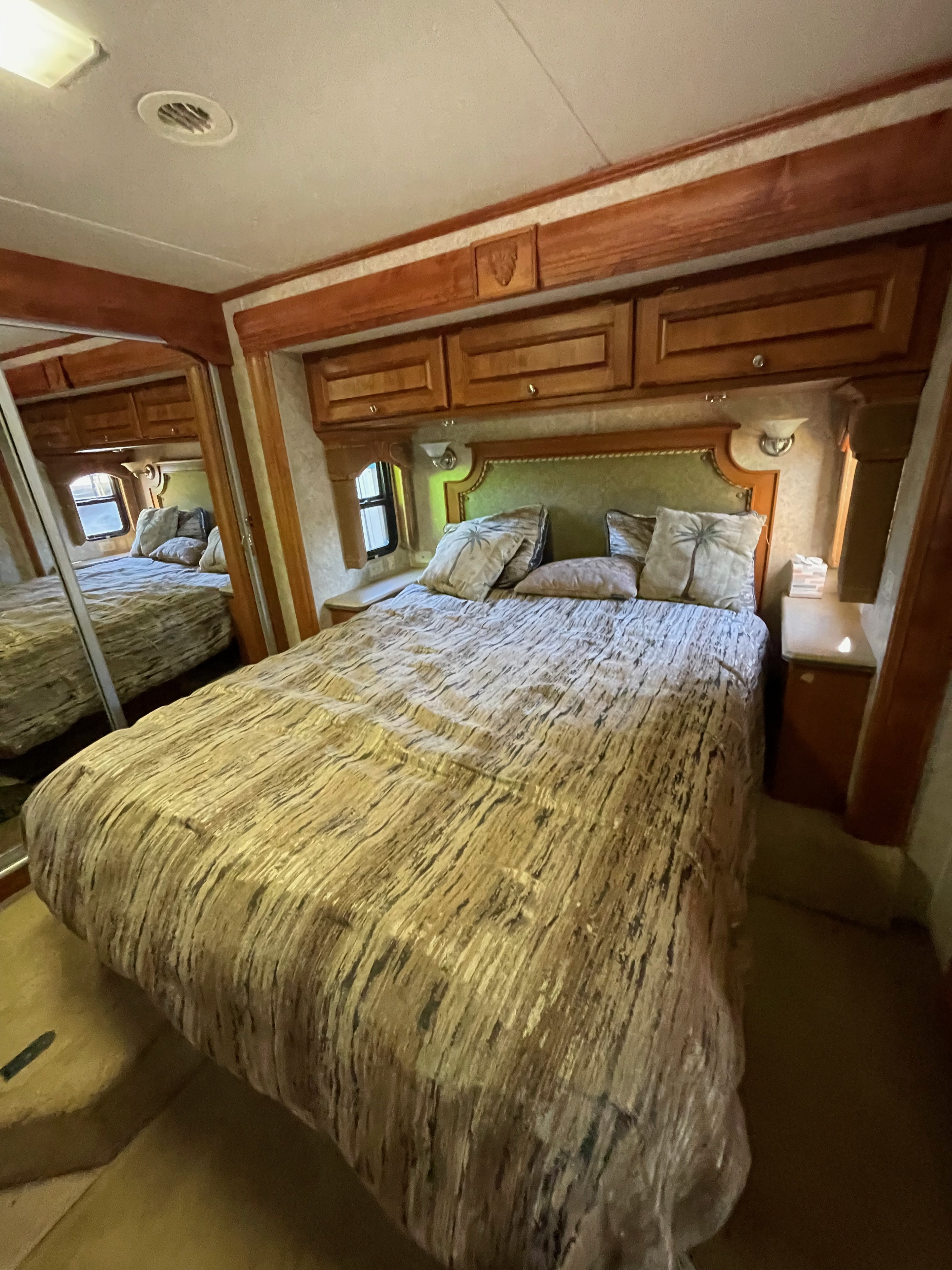 RV rental bedroom: A comfortable bed with textured comforter, green headboard, wooden cabinets, & mirrored wardrobe.. Monaco Diplomat 2006