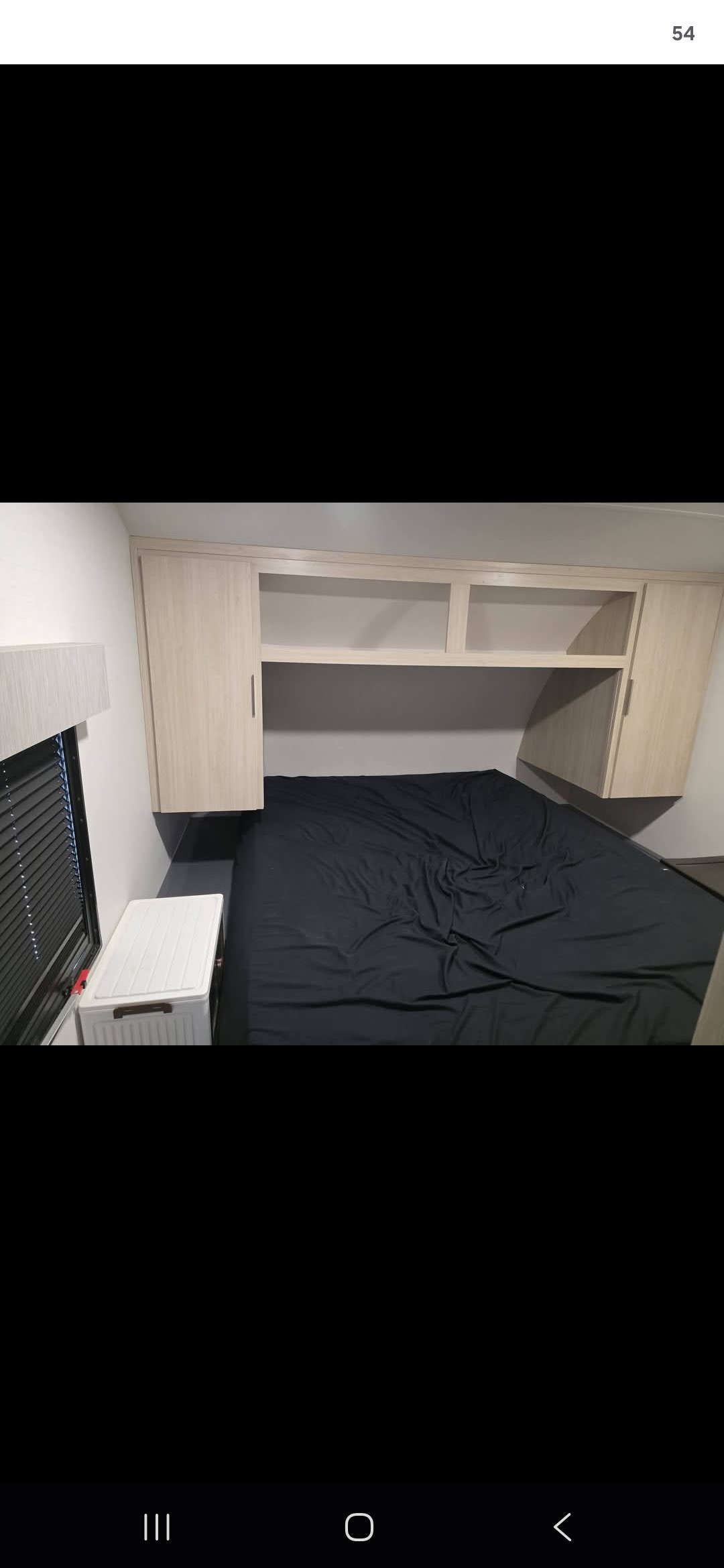 RV rental bedroom: black bed, light wood overhead storage, and window. Ideal for compact travel accommodation.. Forest River Tracer Ultra Lite 2025