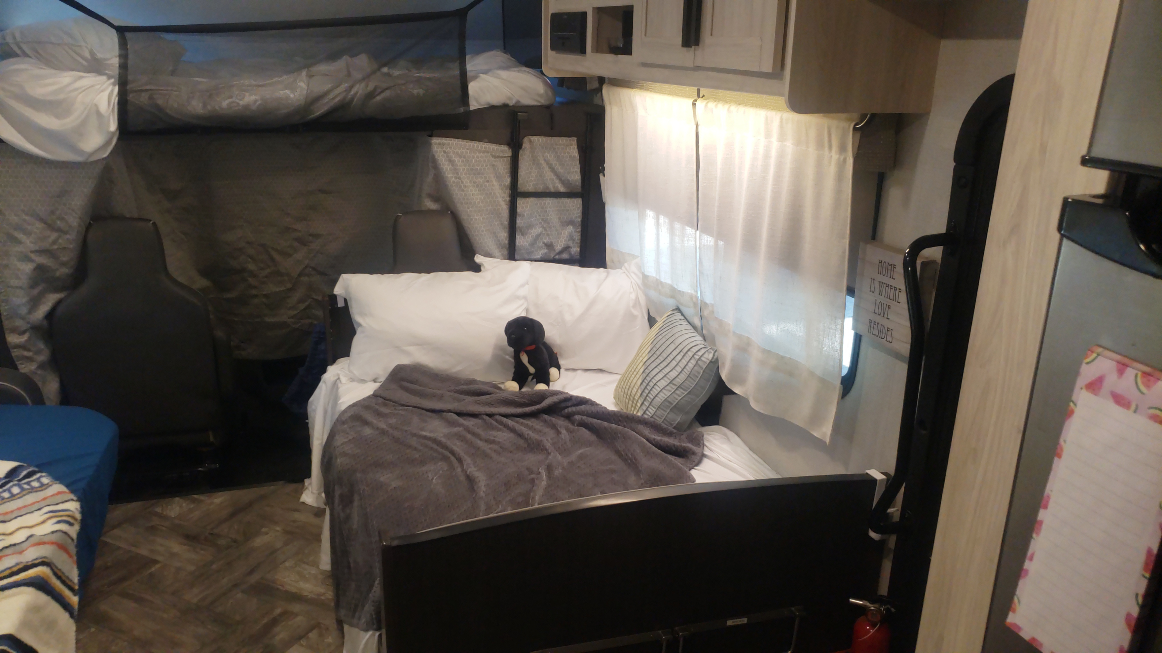 RV rental bedroom: main bed with a stuffed dog, white linens, and bunk beds above. Cozy space with wood-look flooring.. Forest River Sunseeker LE 2022