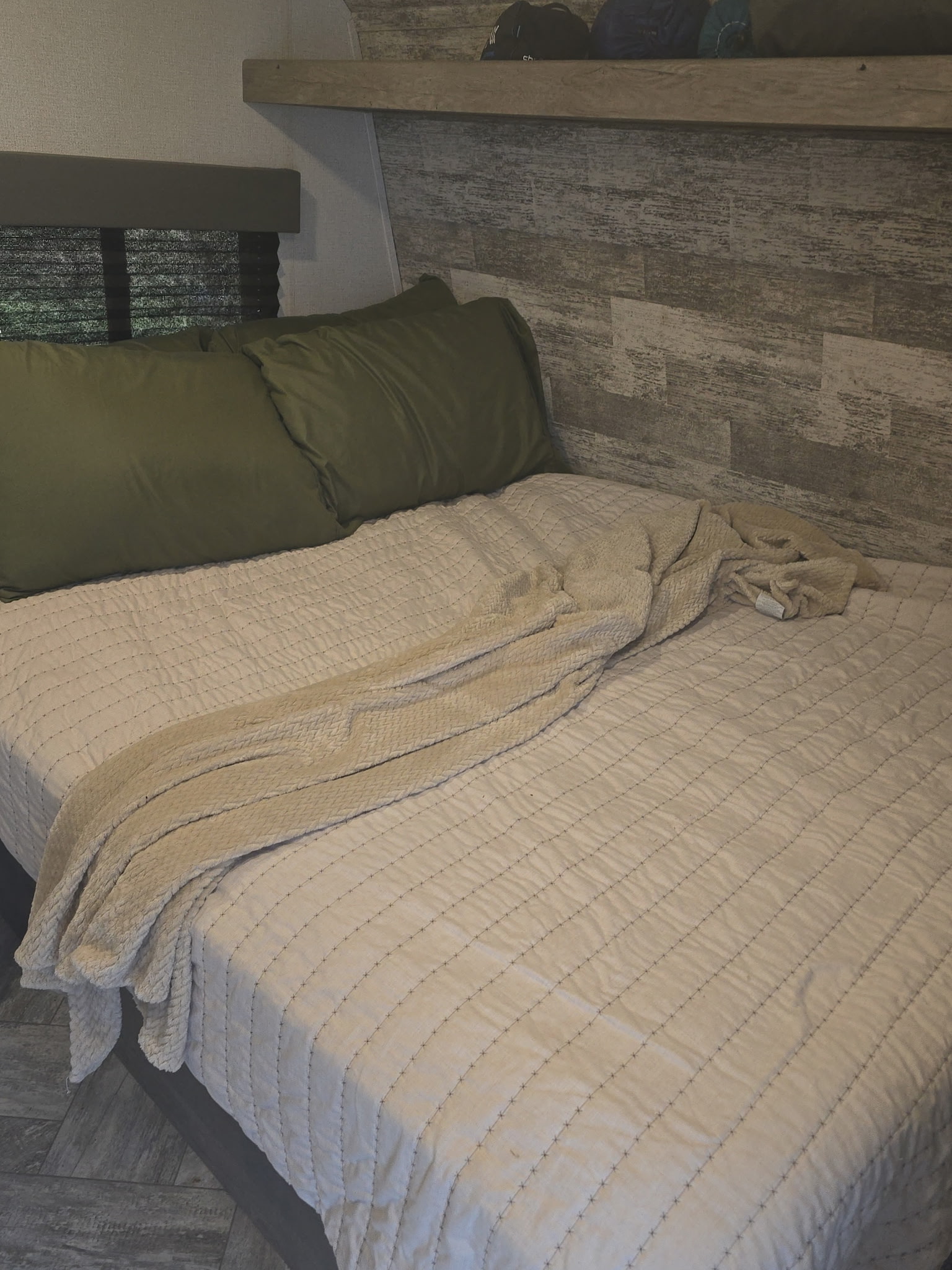 Cozy RV rental bedroom: bed with green pillows, quilted comforter, throw blanket, and storage shelf.. Keystone RV Springdale 2021