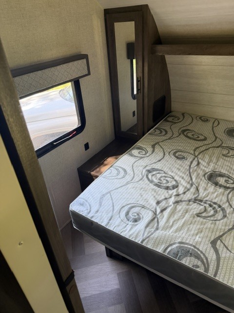 RV rental bedroom interior: A compact space with a patterned bed, window, and mirrored wardrobe.. Forest River Wildwood X-Lite 2021