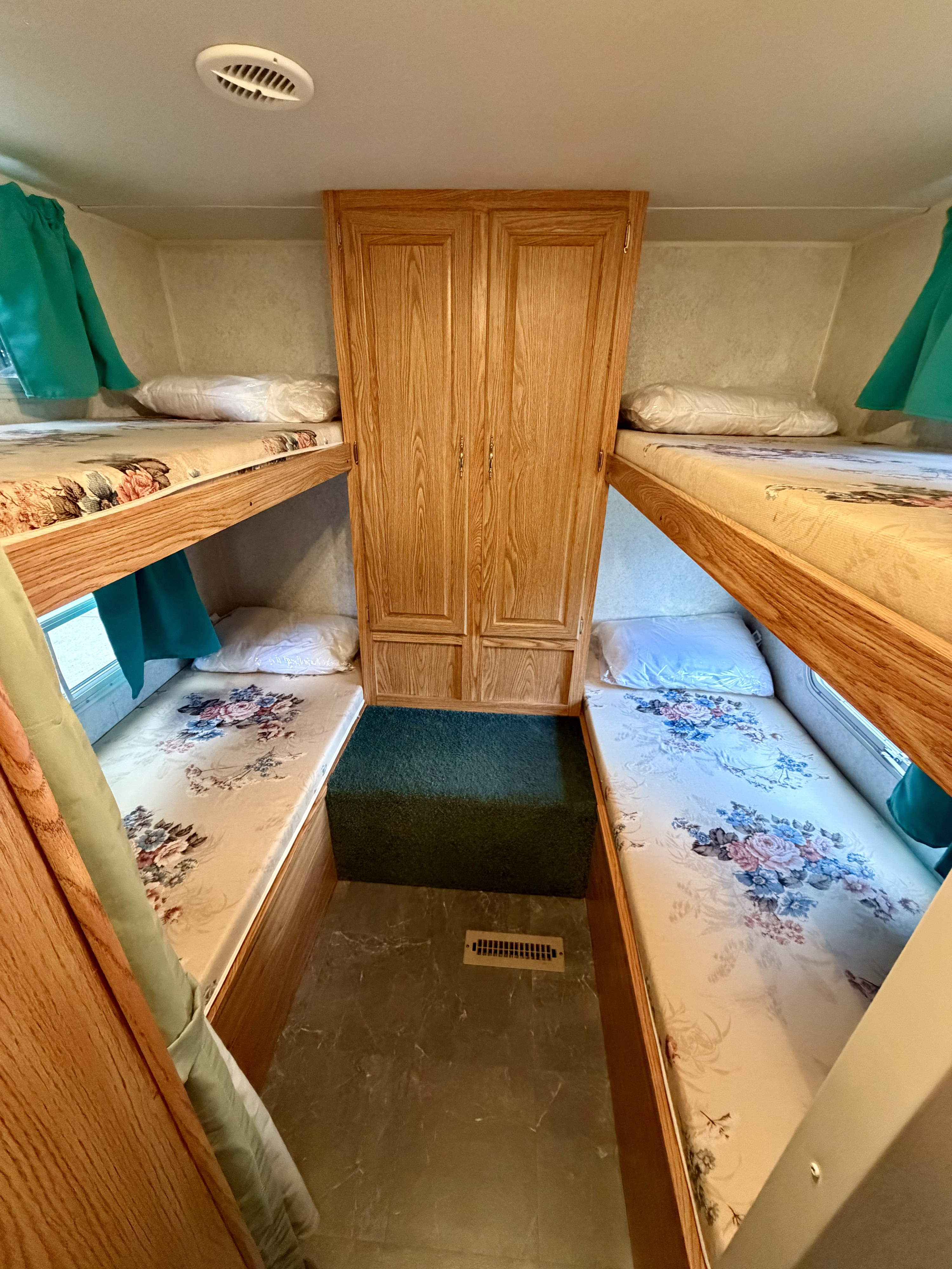 This RV rental offers a compact sleeping area with bunk beds on each side, floral mattresses, and a central wooden cabinet.. Dutchmen Sport 2003